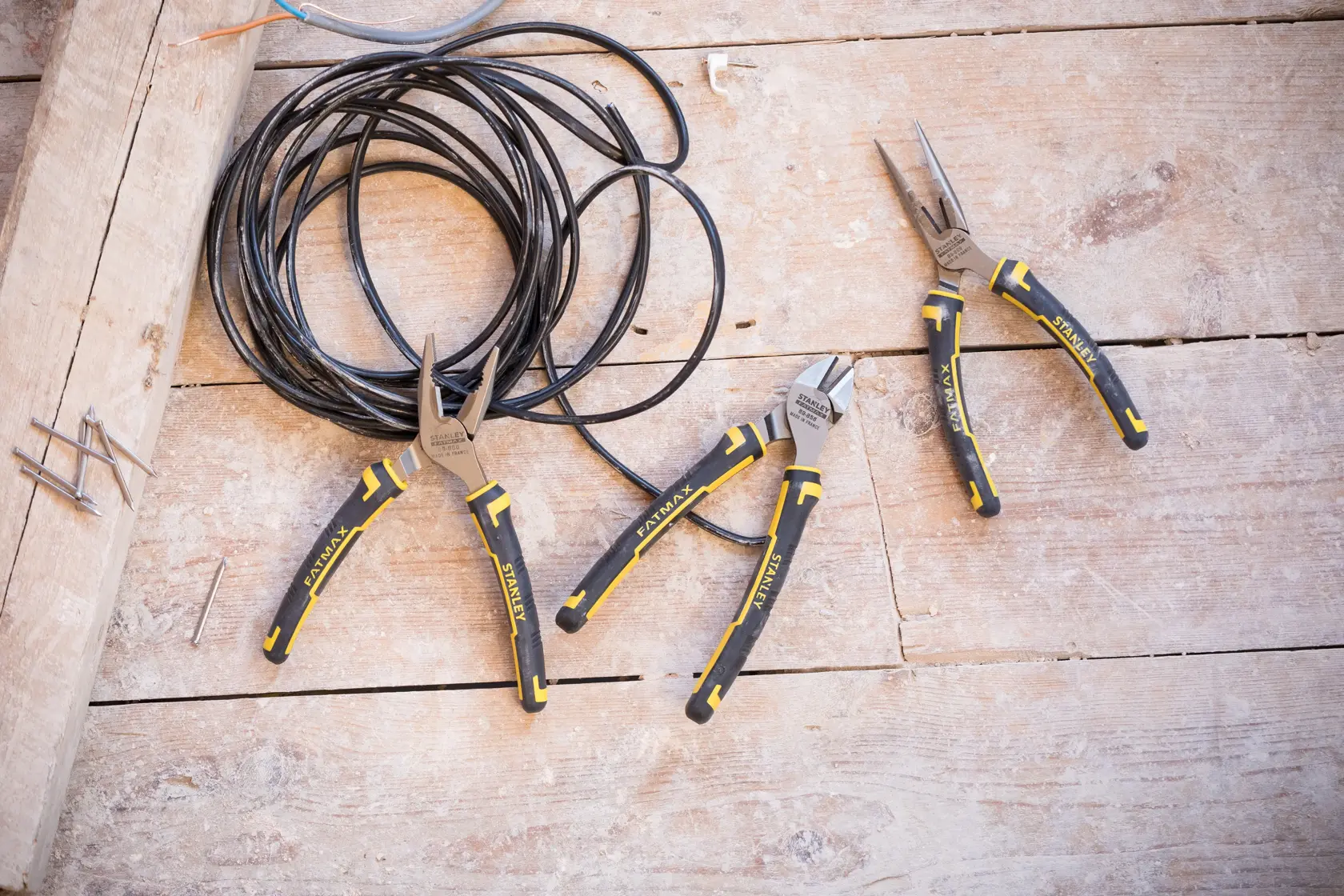 Photo of STANLEY 4-84-488 plier set with black and yellow handles on wooden surface, coiled wire nearby.