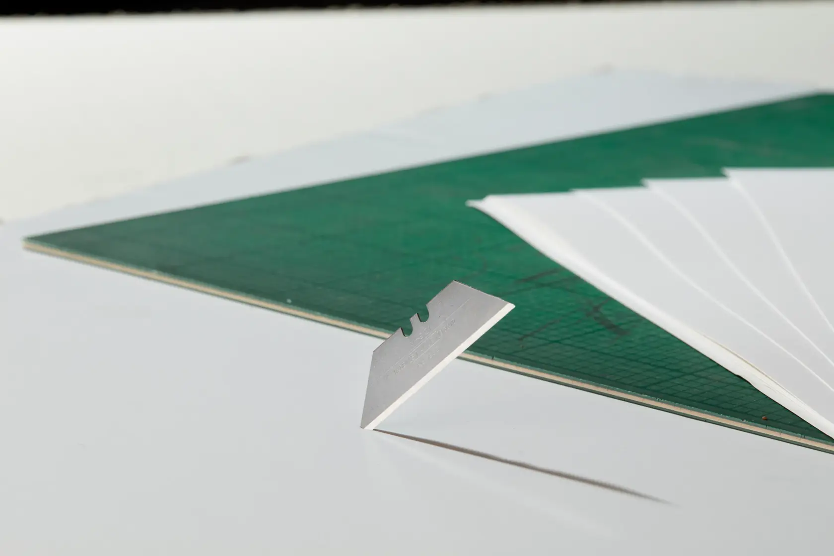 STANLEY 8-11-921 utility razor blade standing on edge next to green cutting mat and white sheets, side view.