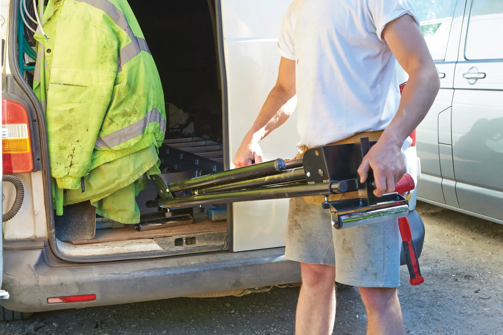 STANLEY FME790-XJ tripod stand, black metal, being carried by a worker near a van.