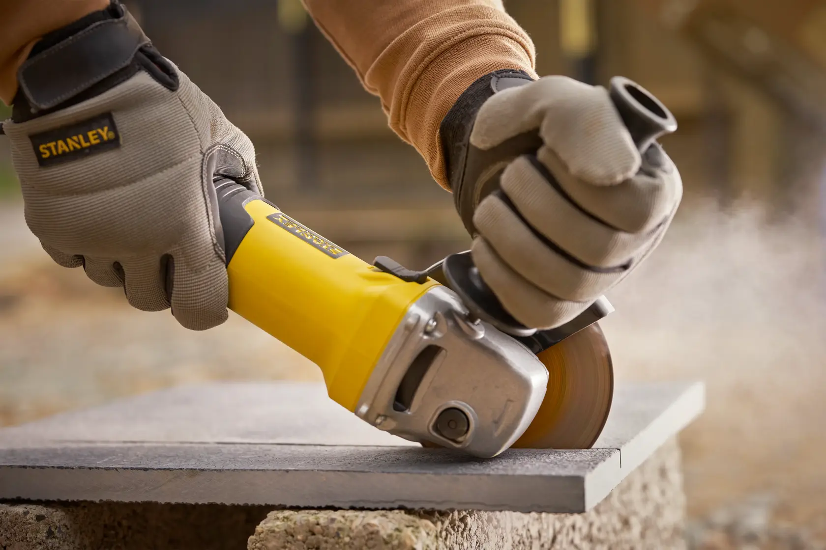 Photo of STANLEY FMEG225VS grinder cutting stone slab outdoors, worker wearing protective gloves.