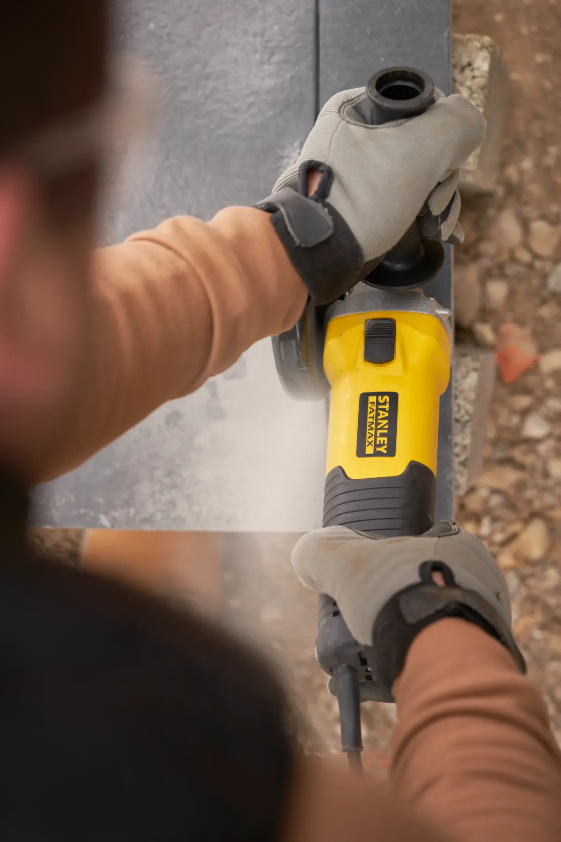 Photo of STANLEY FMEG225VS angle grinder used on stone by gloved hands outdoors.