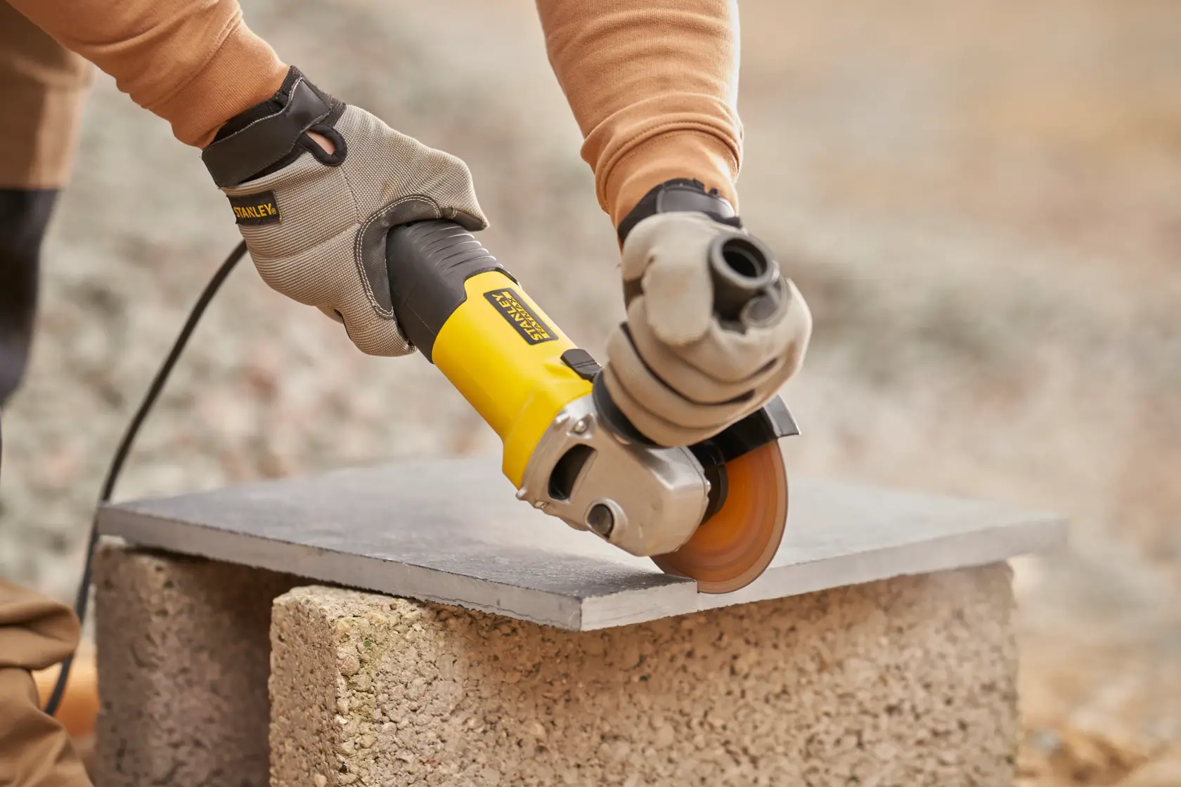 Photo of STANLEY FMEG225VS angle grinder cutting stone slab outdoors, operator wearing work gloves.