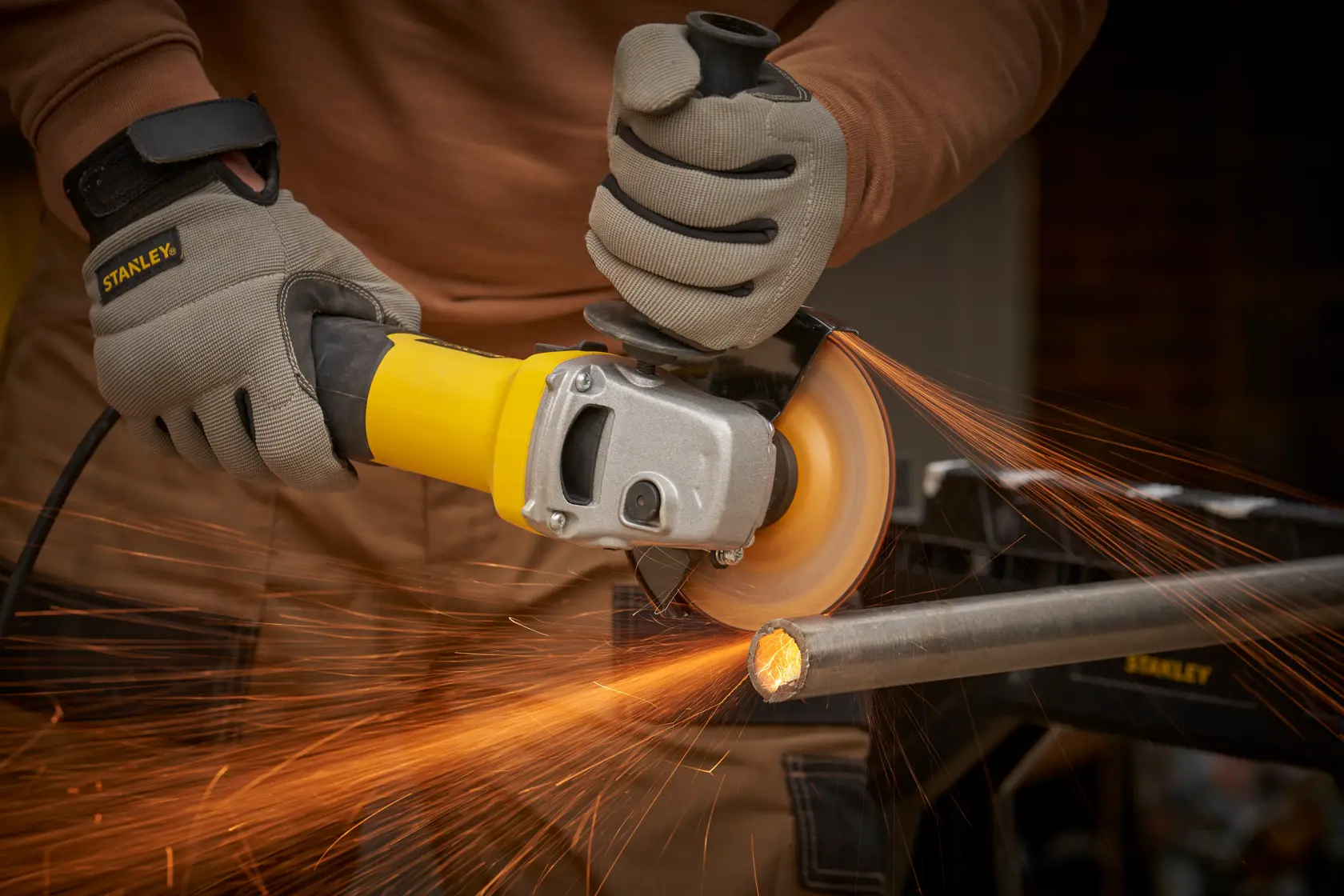 STANLEY FMEG225VS angle grinder cutting metal pipe, close-up with sparks flying.