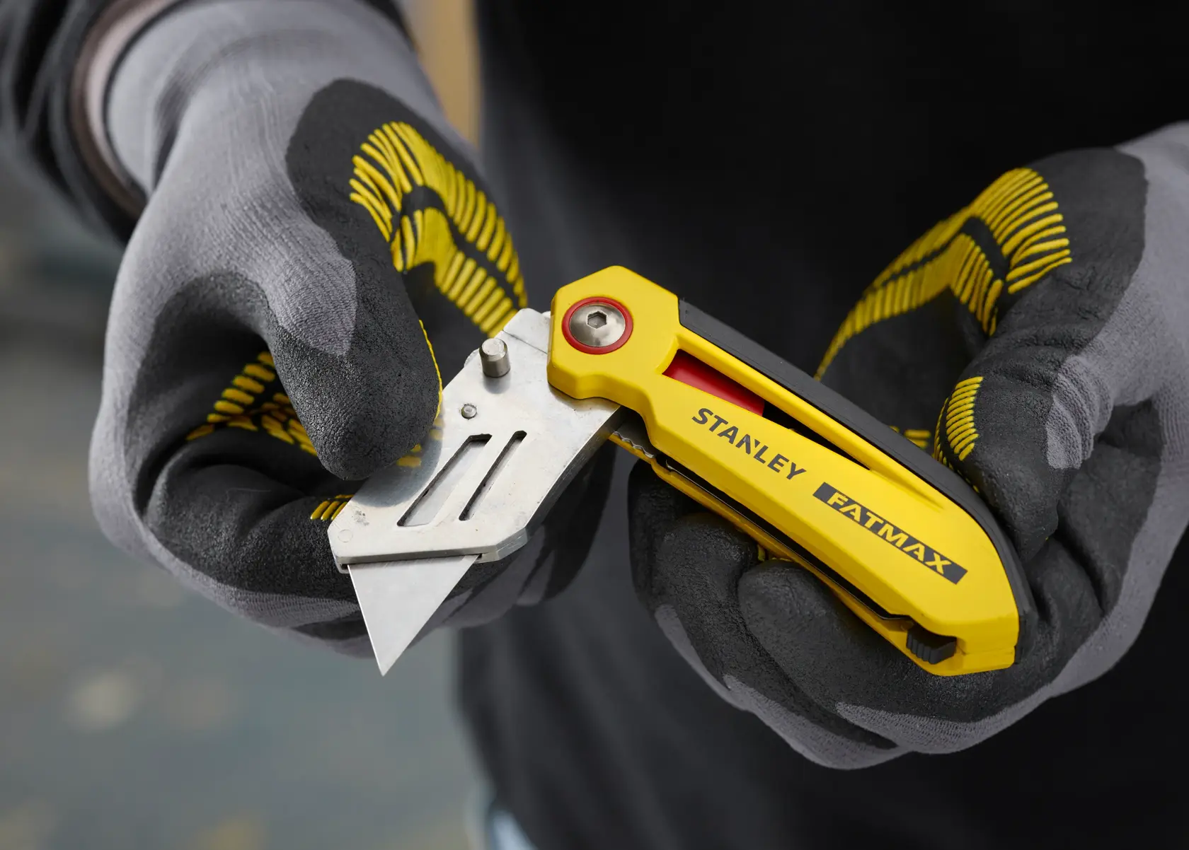 STANLEY FMHT0-10827 yellow folding utility knife held in gloved hands, close-up.