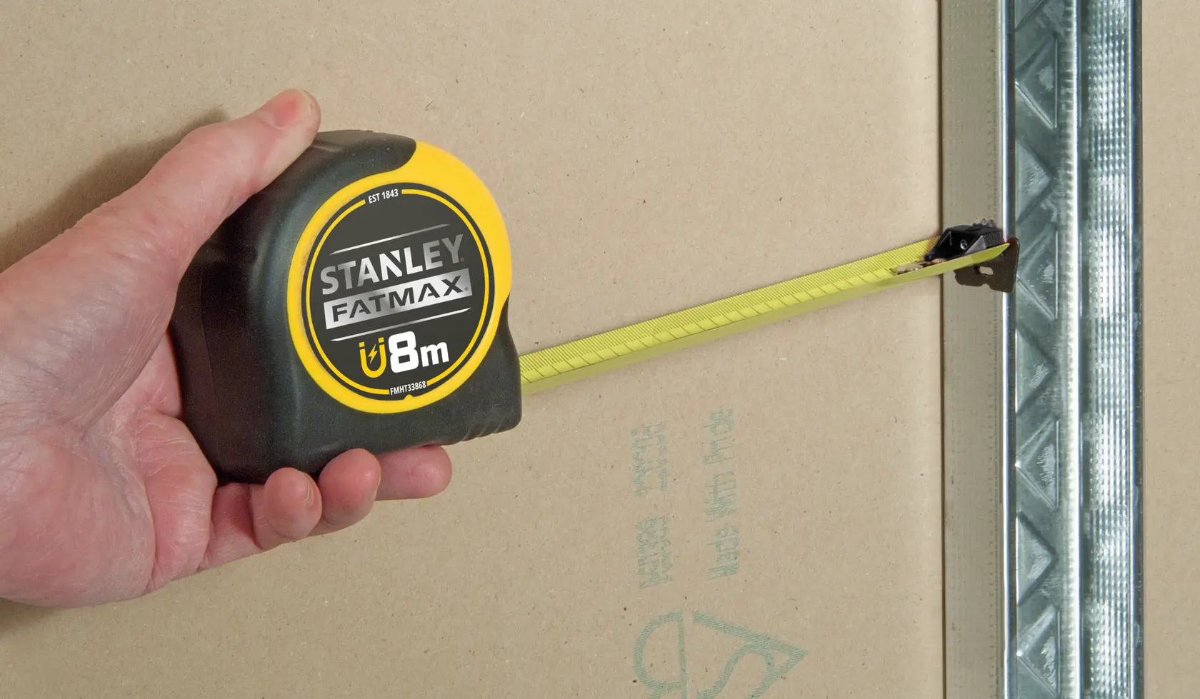 Photo of STANLEY FMHT0-33868 FATMAX 8m tape measure being used to measure on a wall near metal framing.