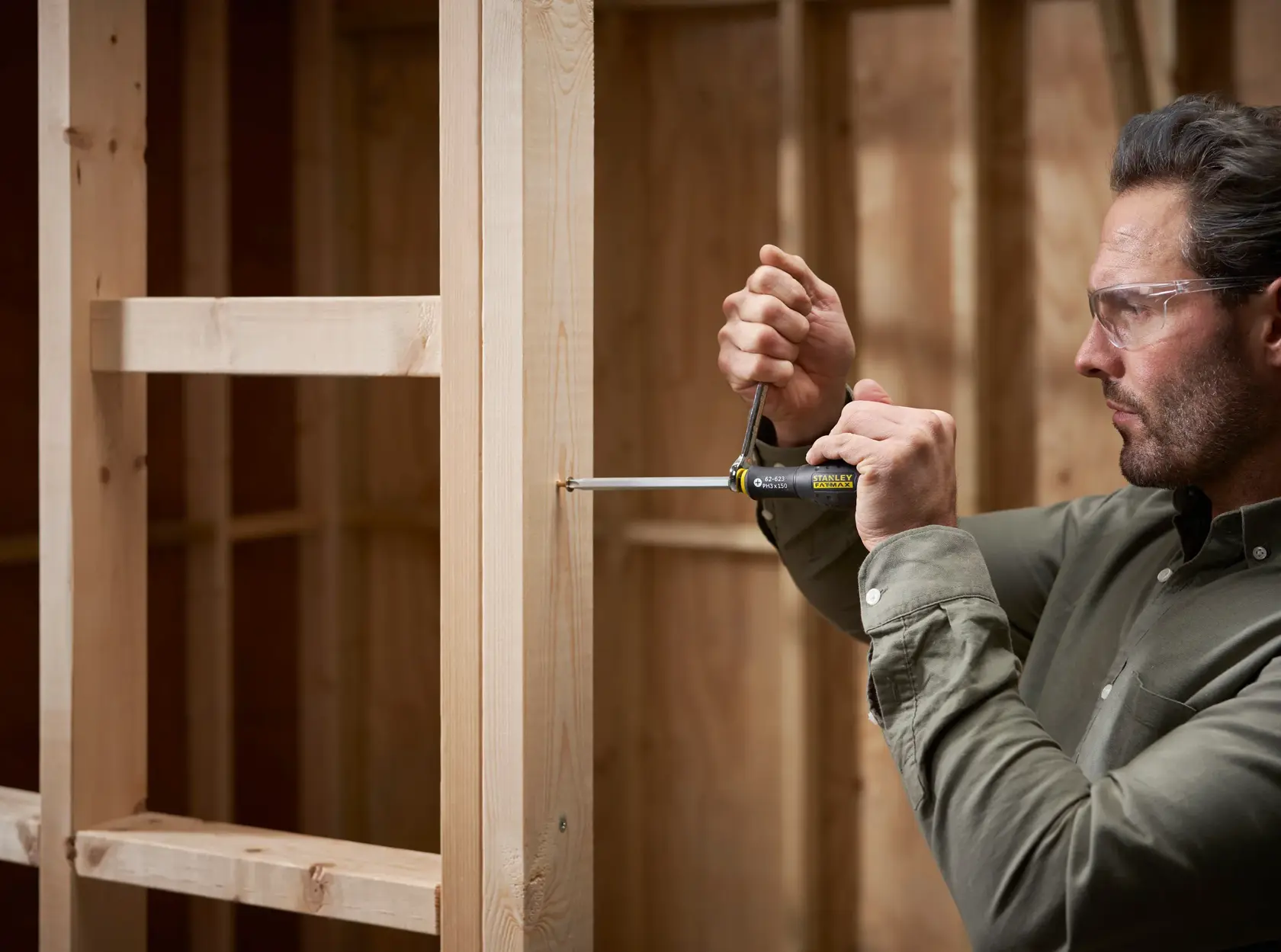 Photo of a person using a STANLEY FMHT0-62623 multi-bit screwdriver on a wooden frame structure, side view.