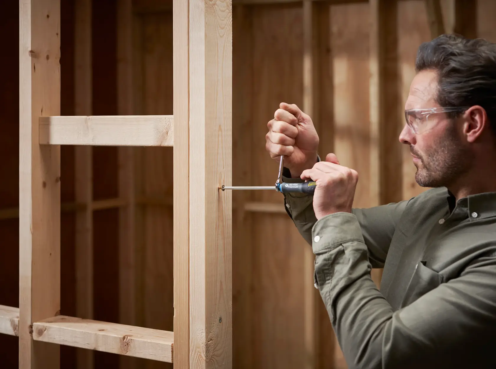 Photo of man using STANLEY FMHT0-62624 screwdriver on wooden frame indoors.
