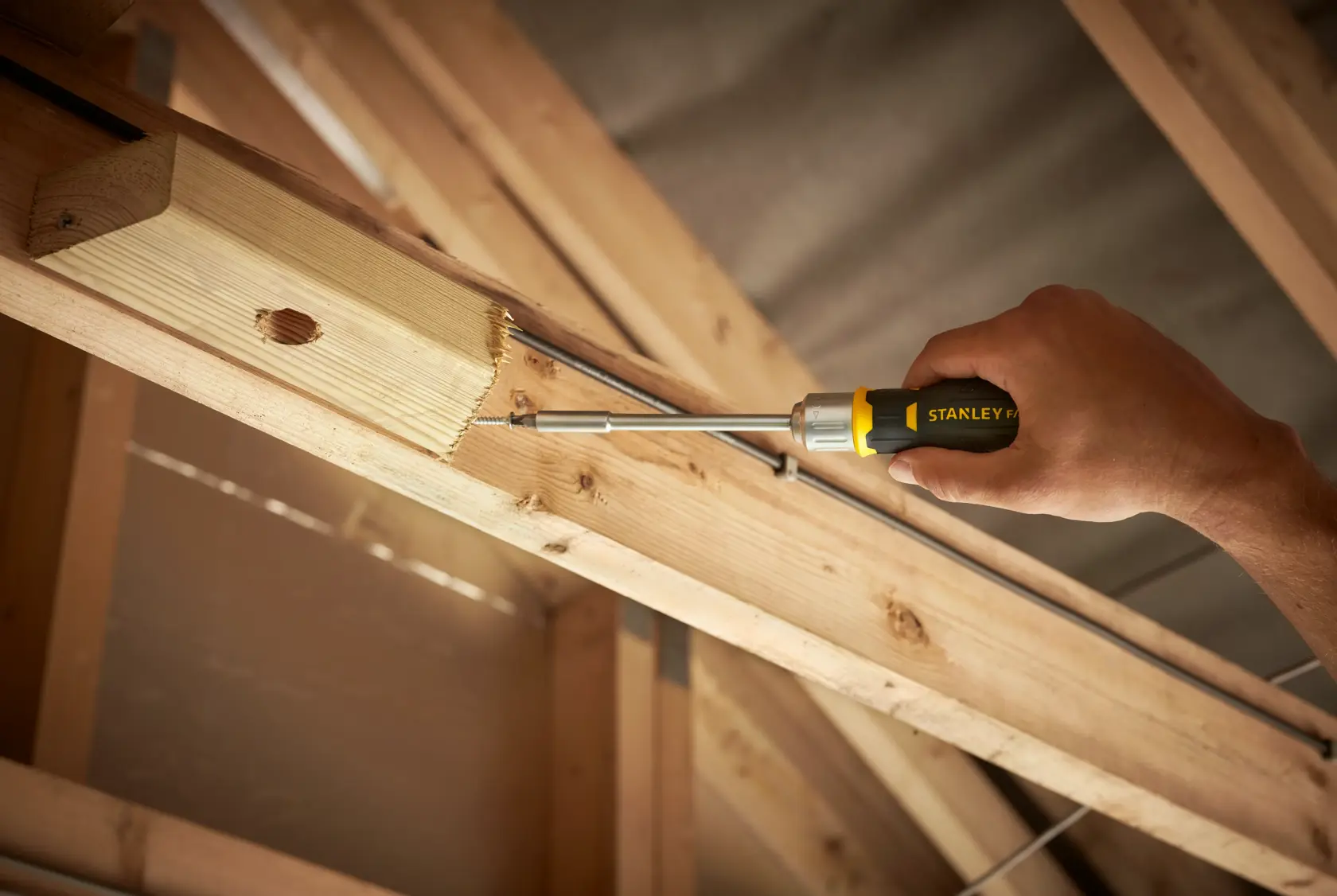 Stanley FMHT0-62690 screwdriver used to fasten screw into wooden beam, closeup in construction setting.