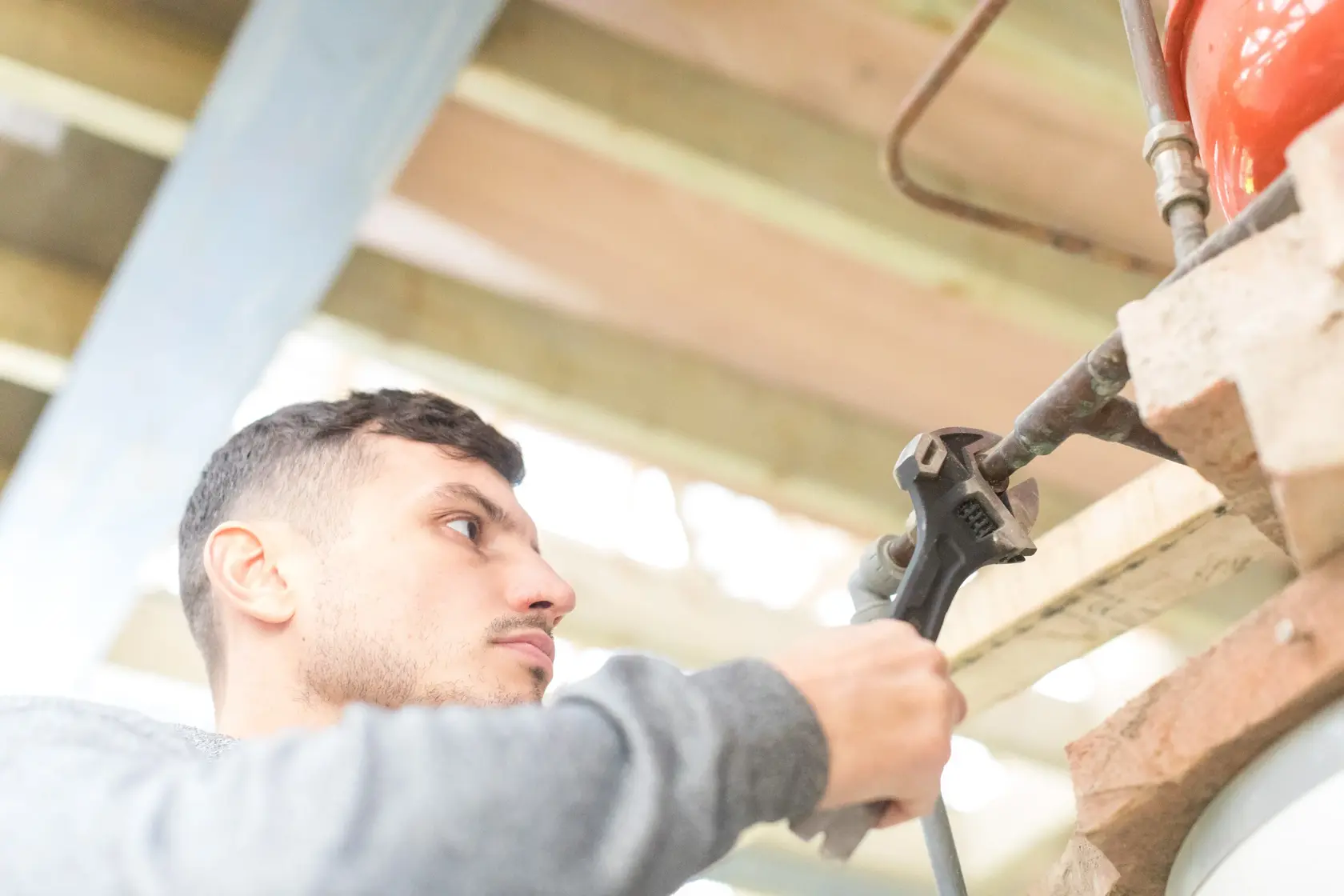 STANLEY FMHT0-75081 adjustable wrench held by a person tightening a pipe in workshop setting.