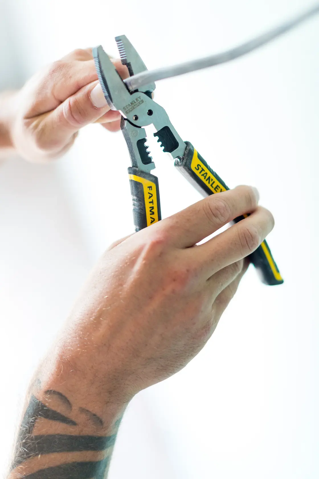 Photo of STANLEY FMHT0-75469 pliers with yellow-black handle cutting a wire, close-up in use.