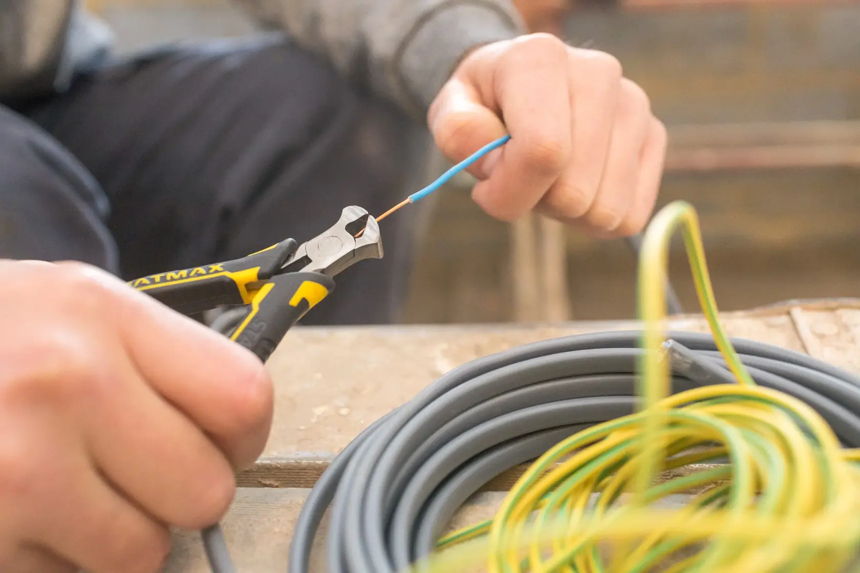 Stanley FMHT0-80519 diagonal pliers cutting blue wire, with coiled cables on a workbench, close-up photography.