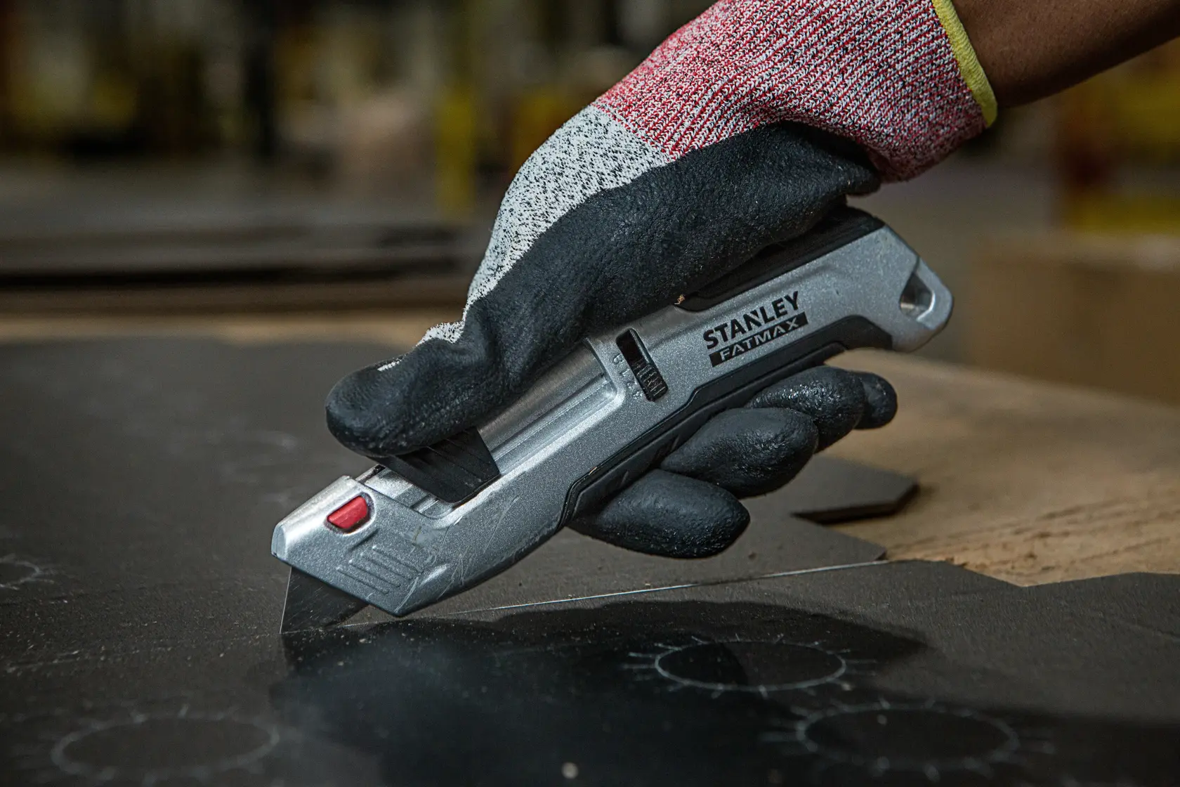 Photo of STANLEY FMHT10367-0 utility knife in gloved hand cutting black material.