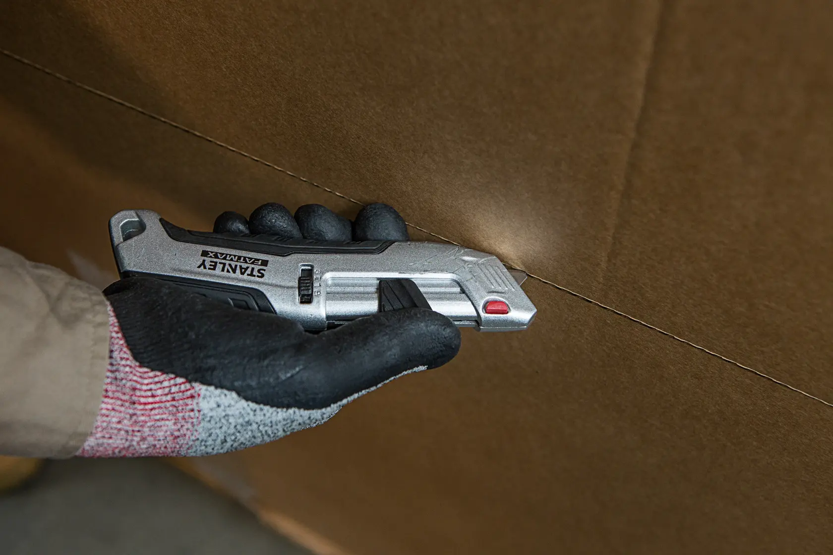 STANLEY FMHT10367-0 utility knife cutting cardboard, close-up of hand holding tool.