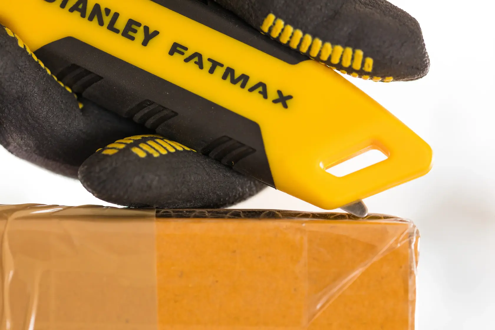 STANLEY FMHT10373-0 utility knife with yellow and black handle, cutting tape on a cardboard box, close-up.