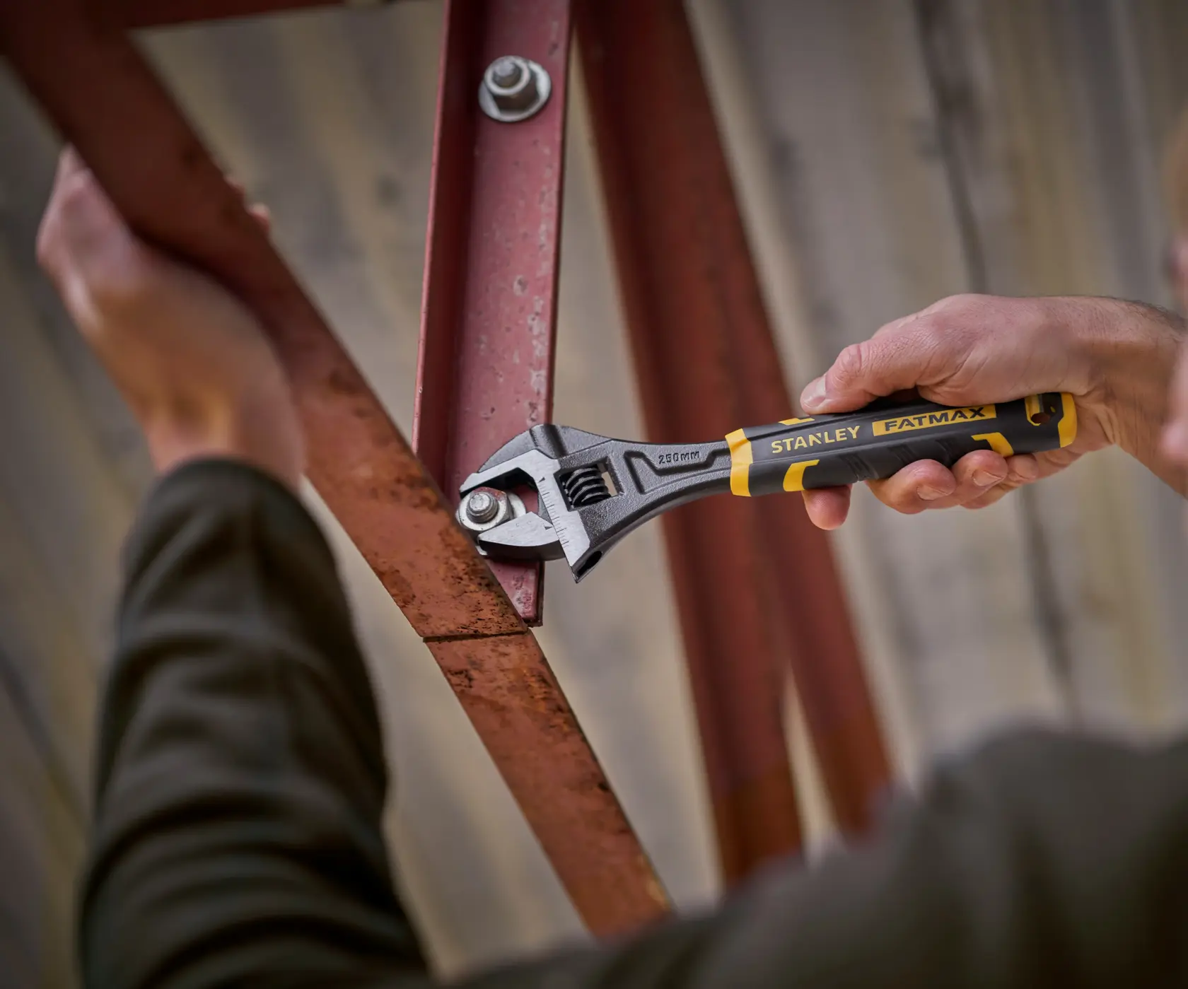 STANLEY FMHT13126-0 adjustable wrench in use tightening a bolt on a red metal frame, close-up photo.