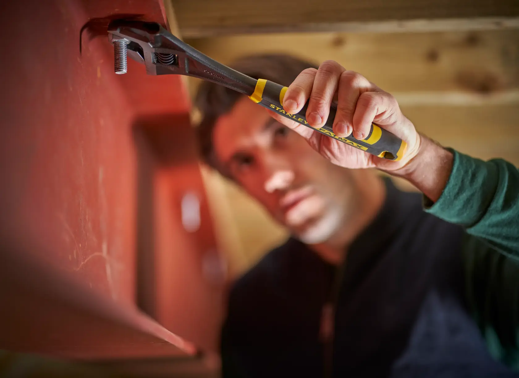 STANLEY FMHT13127-0 adjustable wrench held by hand tightening bolt, close-up photography in workshop setting.