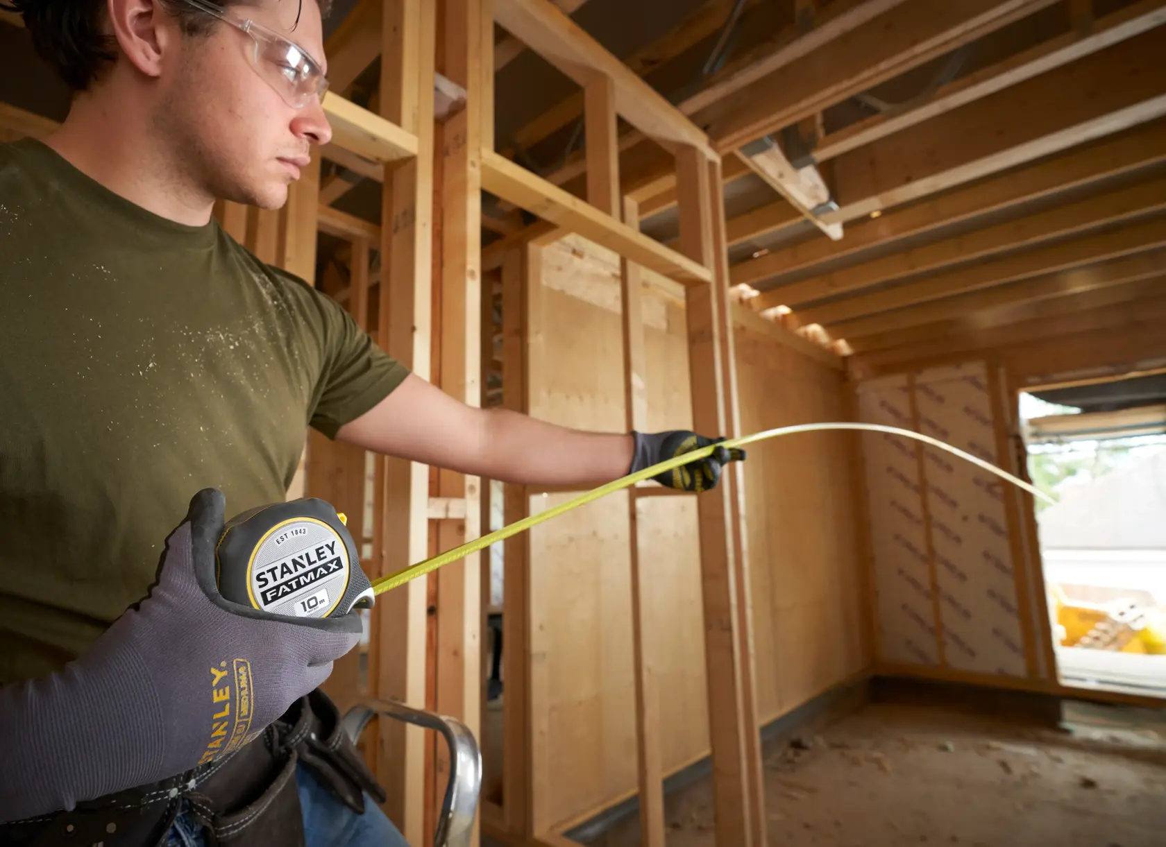 Photo of STANLEY FMHT38232-0 10m tape measure in use at a construction site, extended and held by a gloved worker.