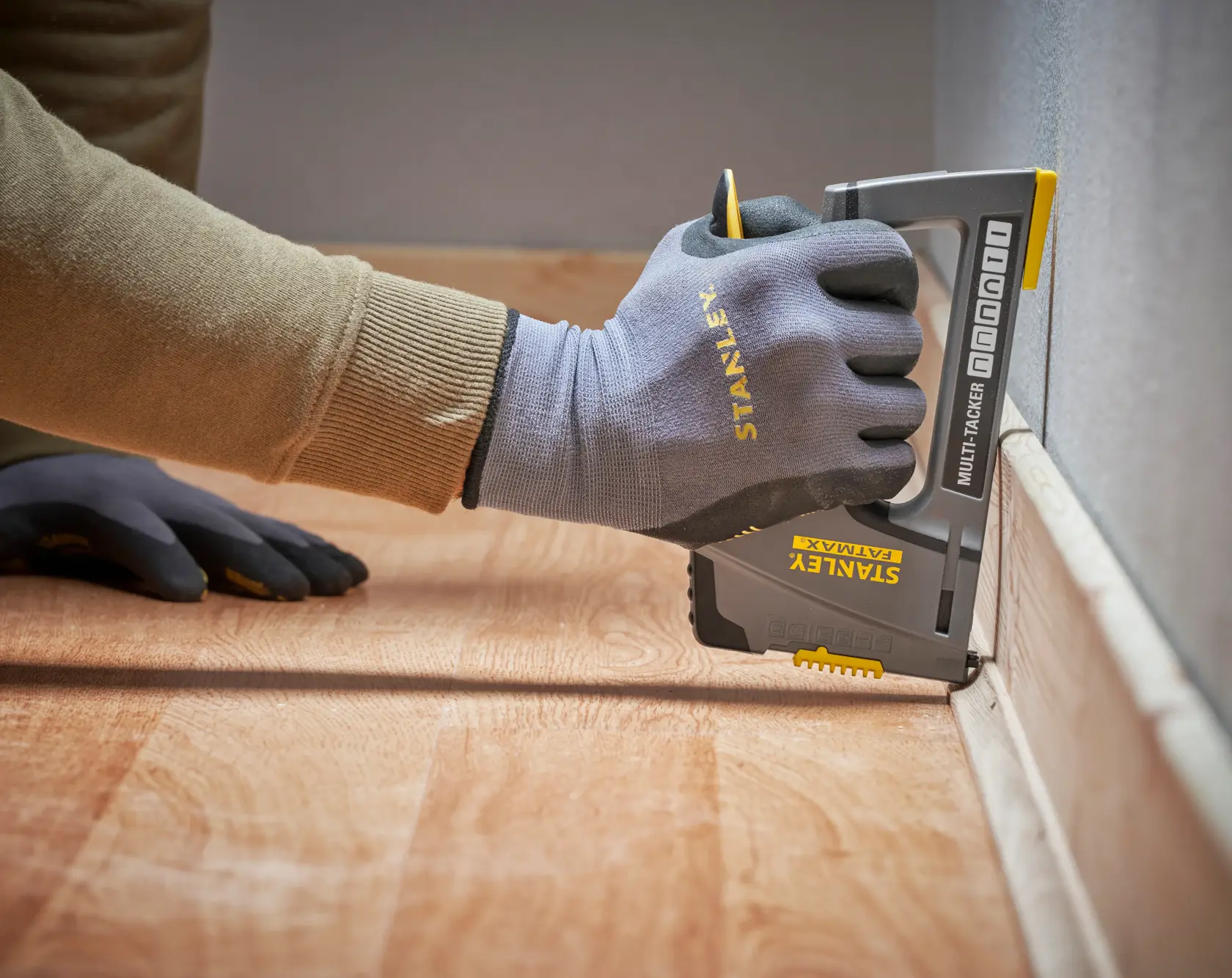 Photo of a hand wearing Stanley gloves using a STANLEY FMHT6-70868 multi-tacker on floor trim, side angle.