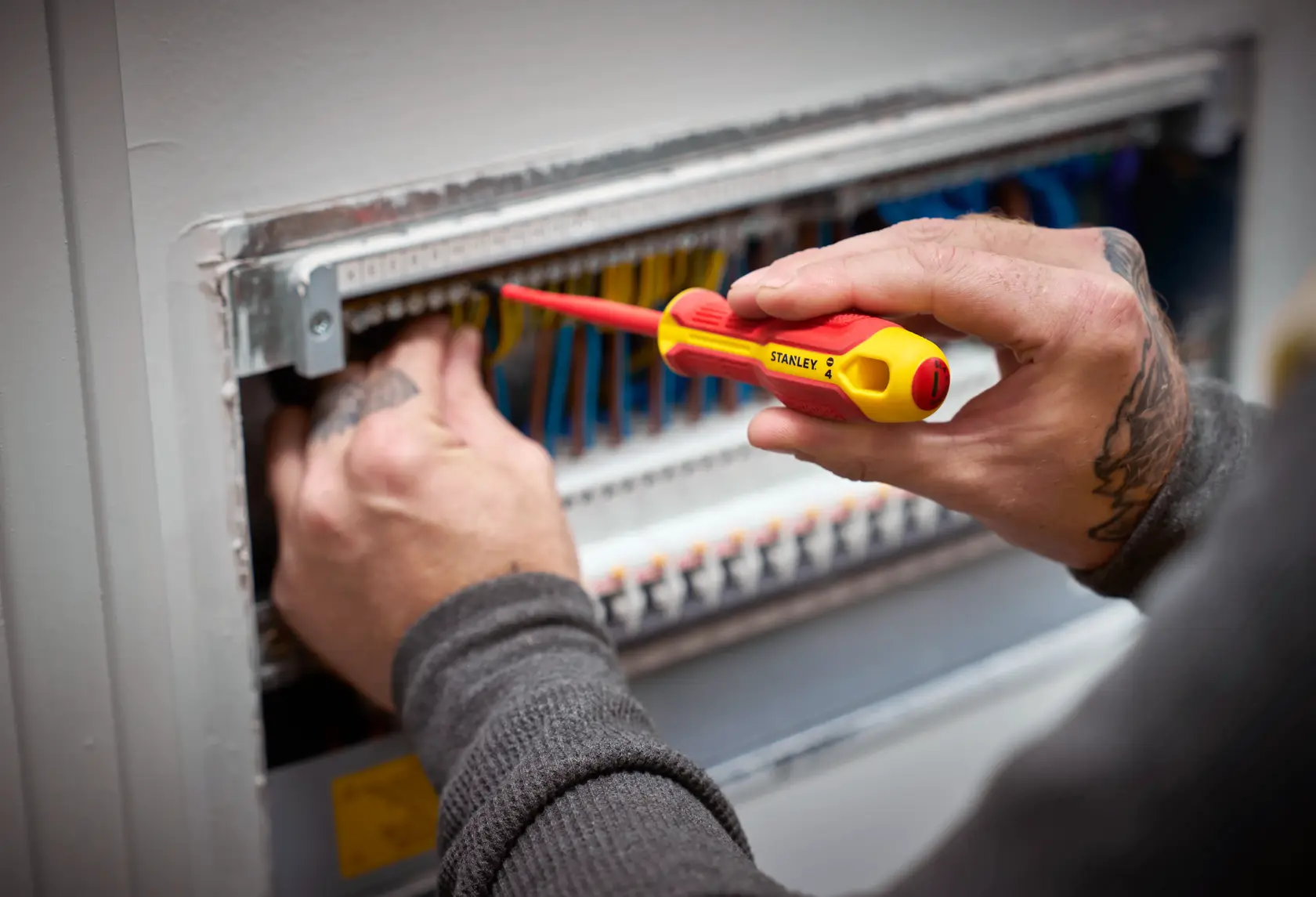 Person uses a STANLEY insulated screwdriver to work on an electrical panel with multiple wires.