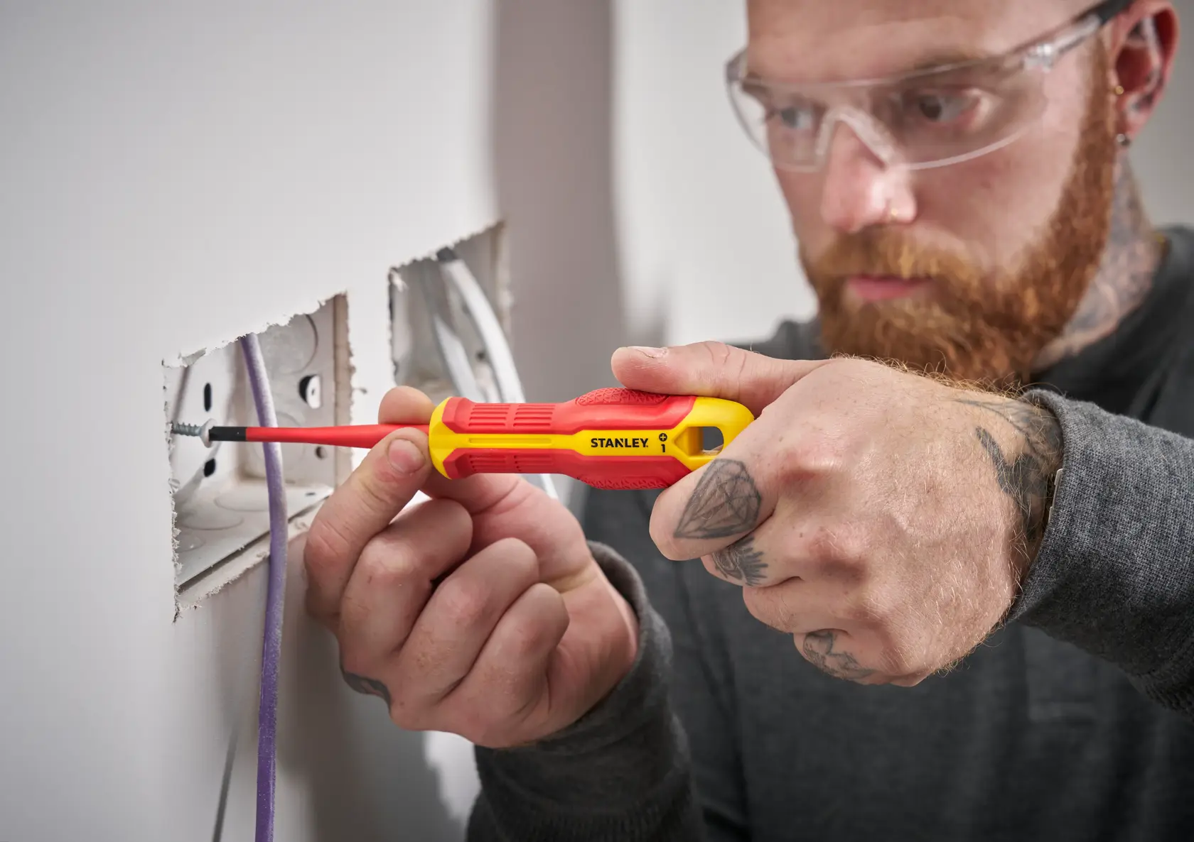 Person uses a STANLEY insulated screwdriver to install a screw in a wall electrical outlet.