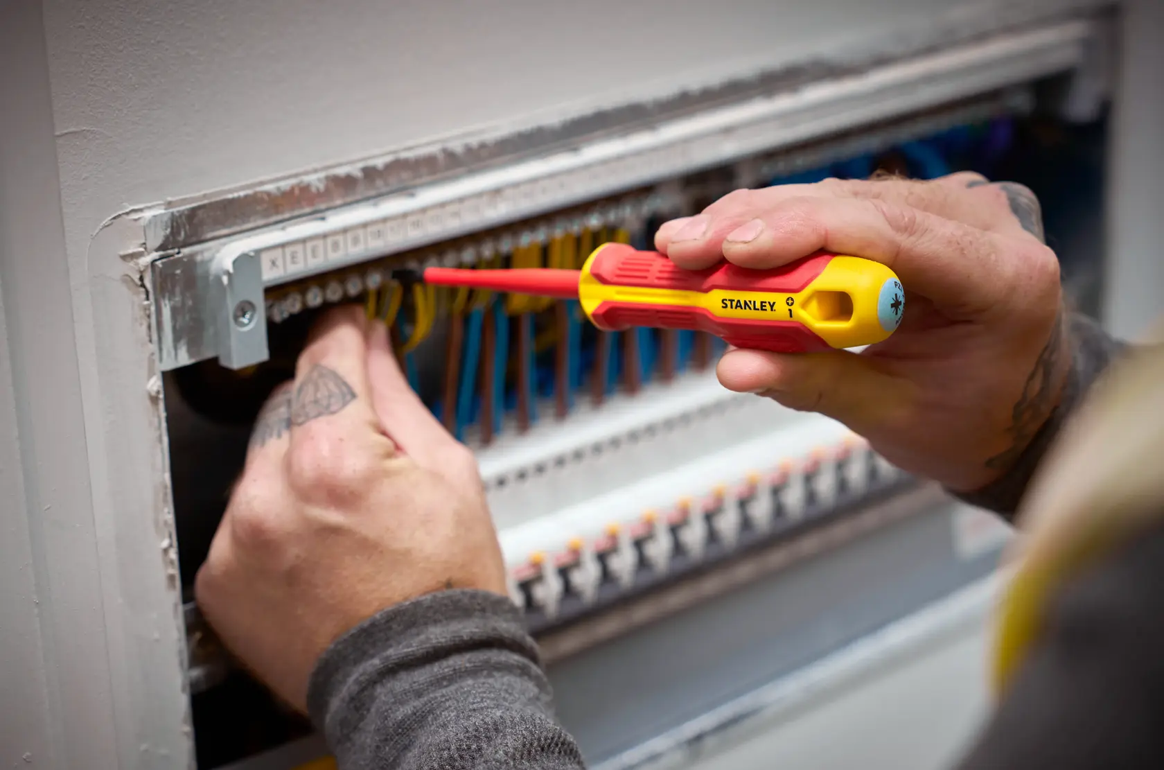 Person uses a STANLEY insulated screwdriver to work on electrical wiring in a control panel.
