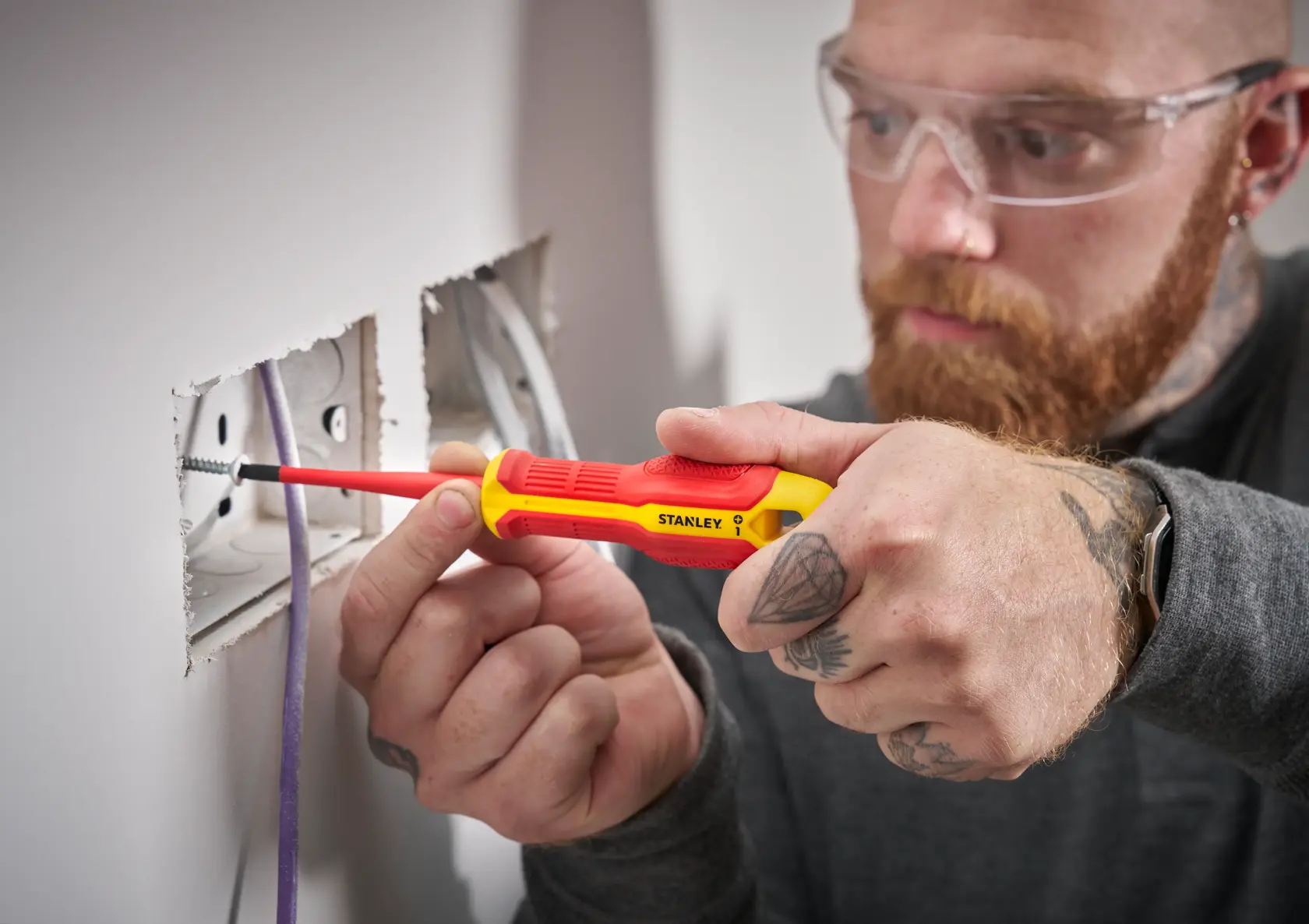 Person uses a STANLEY insulated screwdriver to install or adjust an electrical socket in a wall.