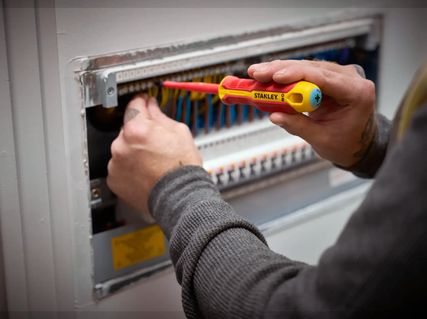 Person uses a STANLEY insulated screwdriver to work on an electrical panel with colorful wires.