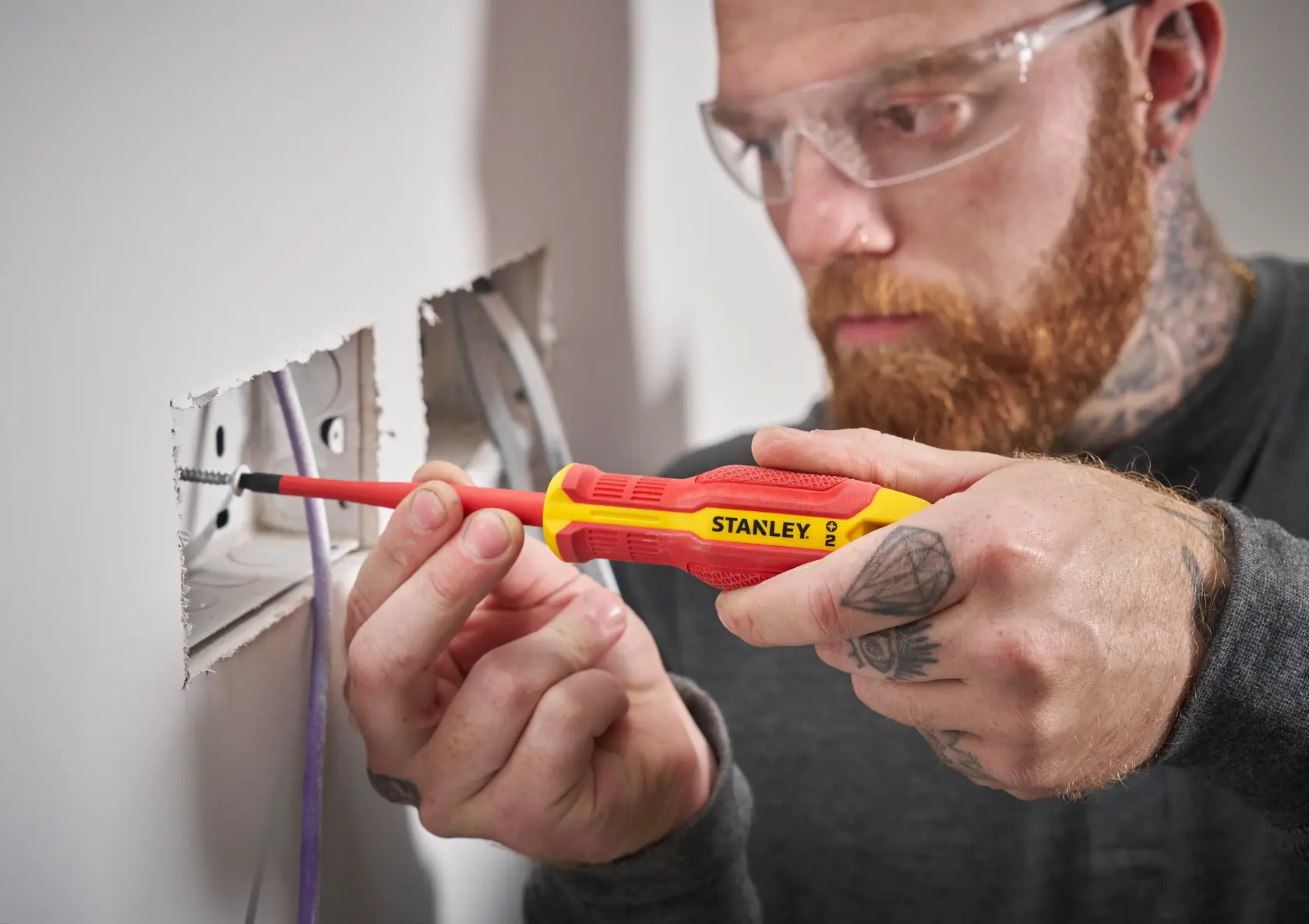 Person uses a Stanley insulated screwdriver to secure wires in an electrical socket on a wall.