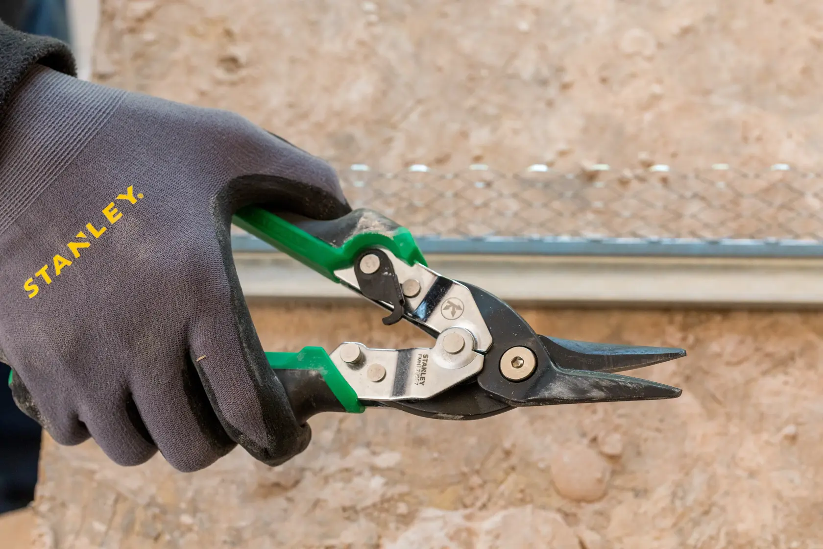 STANLEY FMHT73557-0 green handle aviation snips held in a gloved hand, close-up photo.