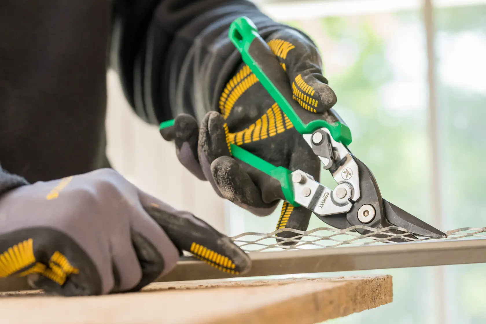 STANLEY FMHT73557-0 aviation snips cutting metal mesh, close-up angle, worker wearing gloves.