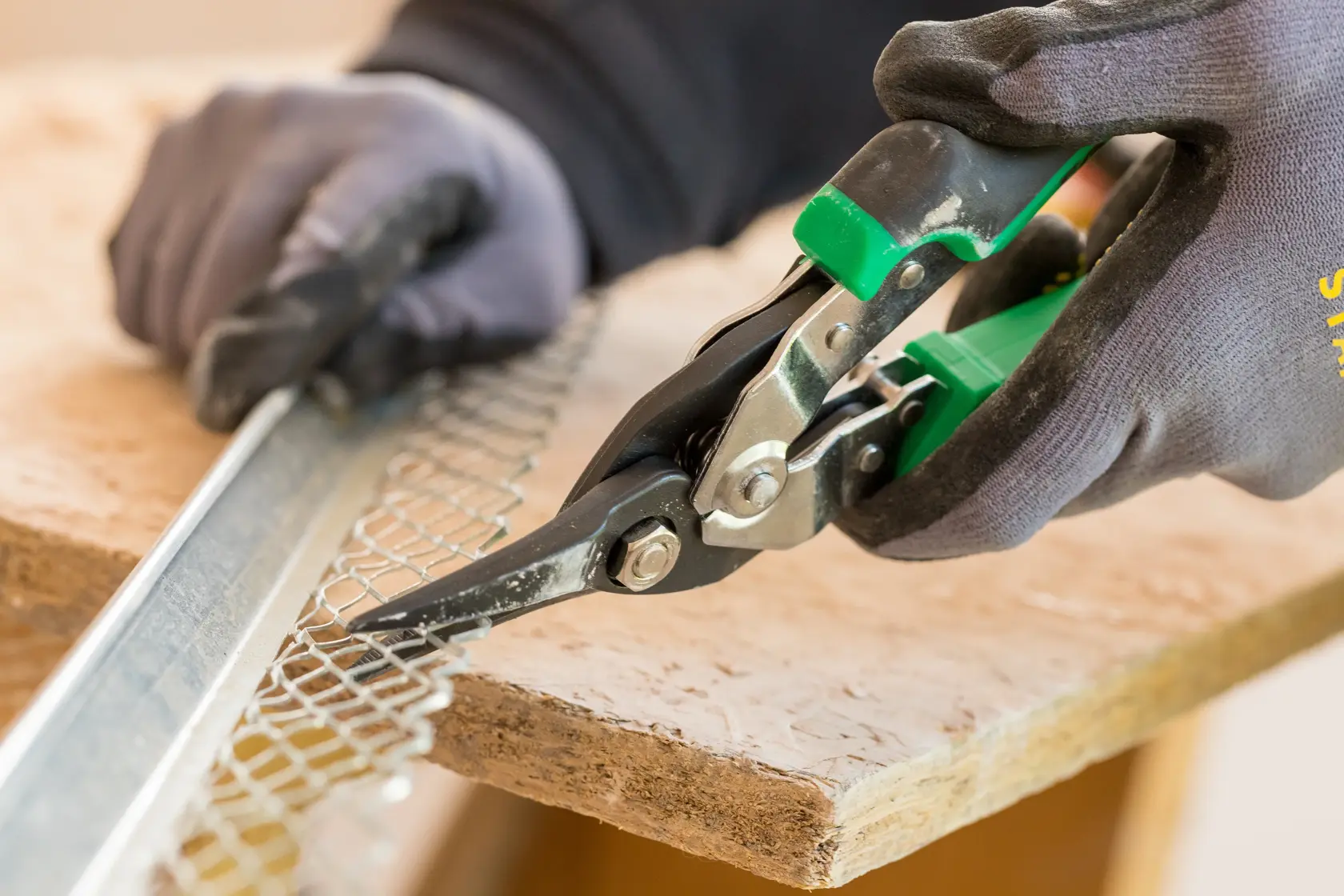 STANLEY FMHT73557-0 aviation snip with green handles held by gloved hand, close-up photo.