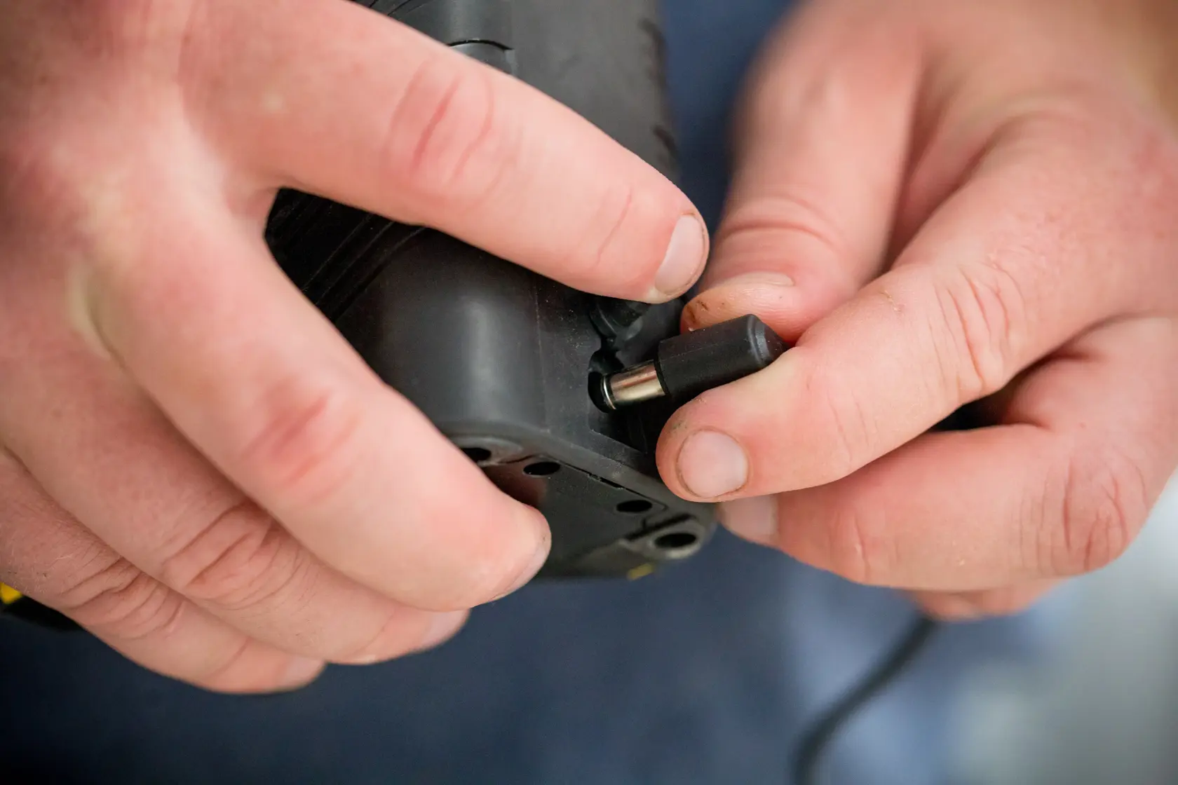 Close-up of hands connecting charger to STANLEY FMHT77597-1 digital laser measure, product photography.