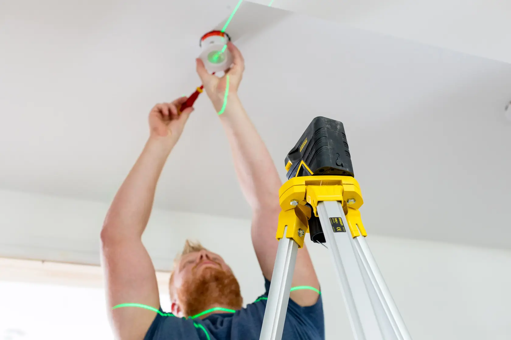 STANLEY FMHT77597-1 laser level tripod in use on ladder, showing green laser lines during ceiling installation.