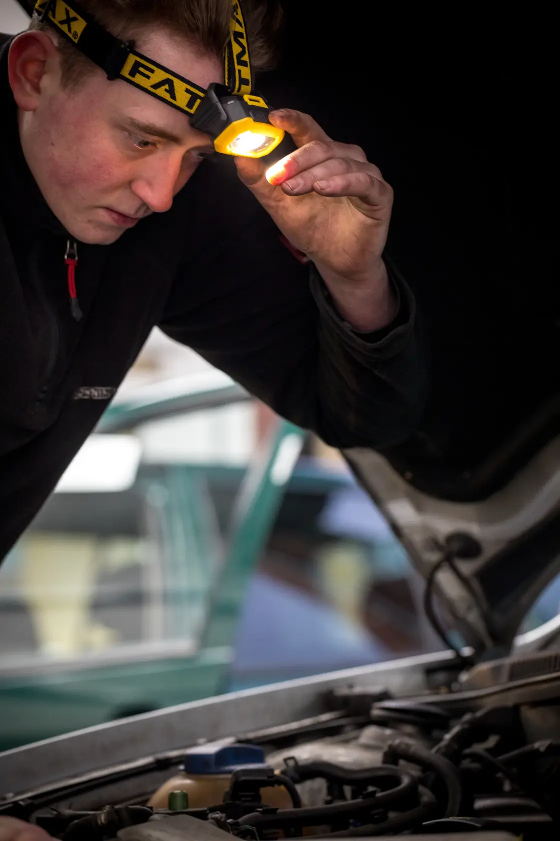 STANLEY FMHT81509-0 headlamp used by person inspecting car engine, close-up photography.