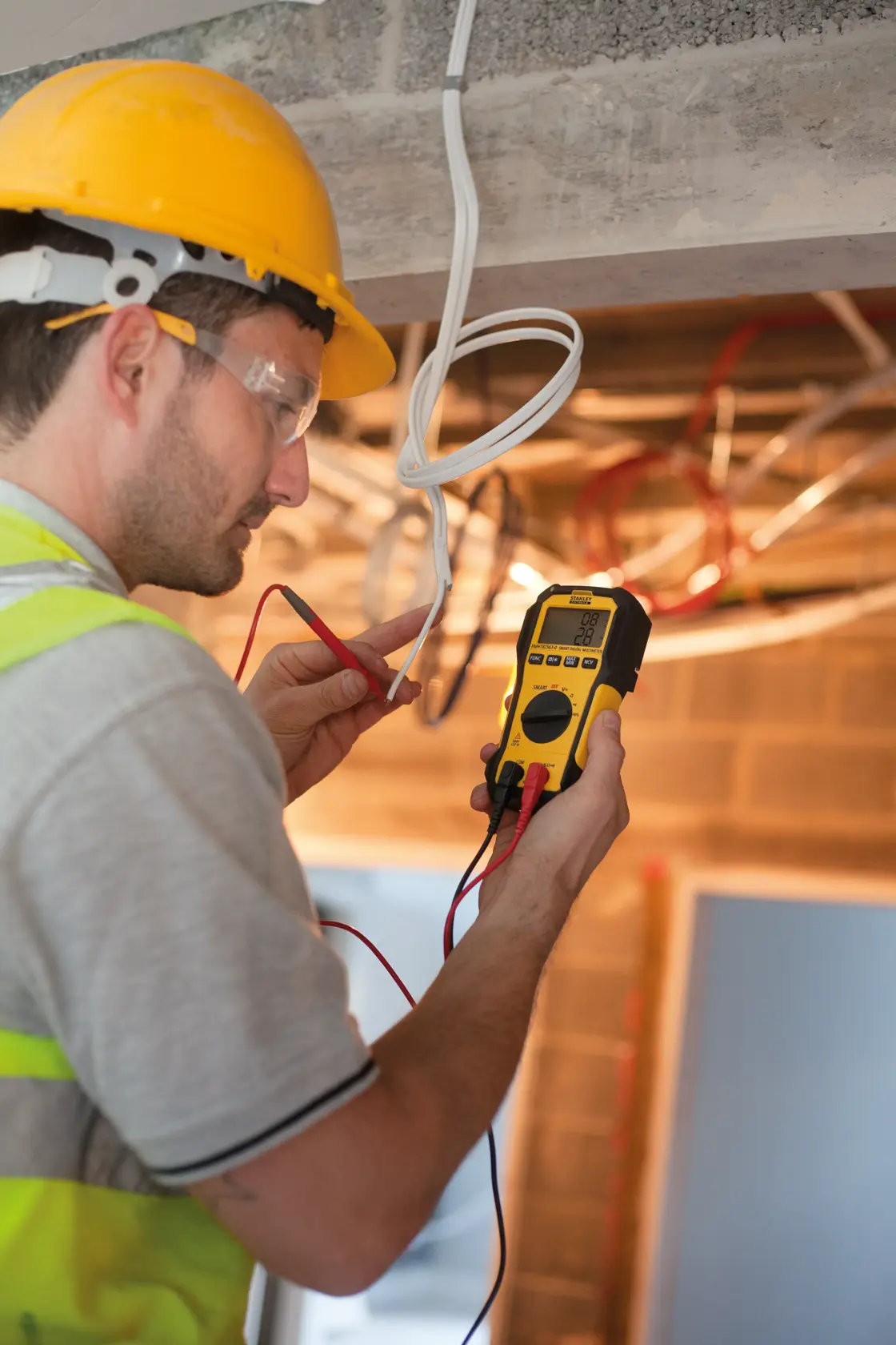 STANLEY FMHT82563-0 digital multimeter used by a worker in a construction setting to test electrical wires.