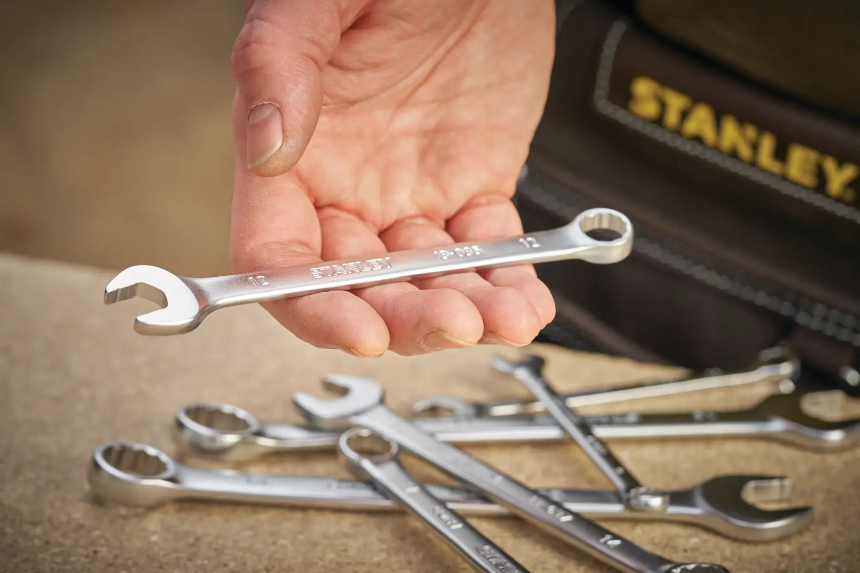 STANLEY FMMT13040-0 spanner held in hand, with several silver wrenches on a work surface, close-up photography.