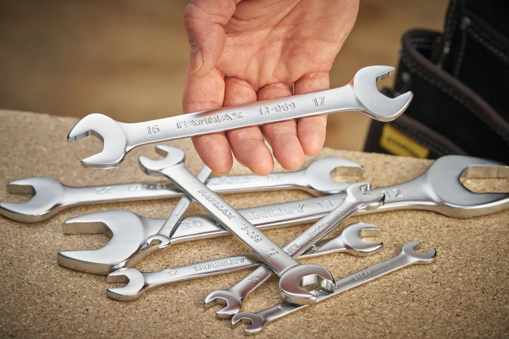 STANLEY FMMT13067-0 spanner set, silver wrenches on workbench, hand holding one wrench, product photography.