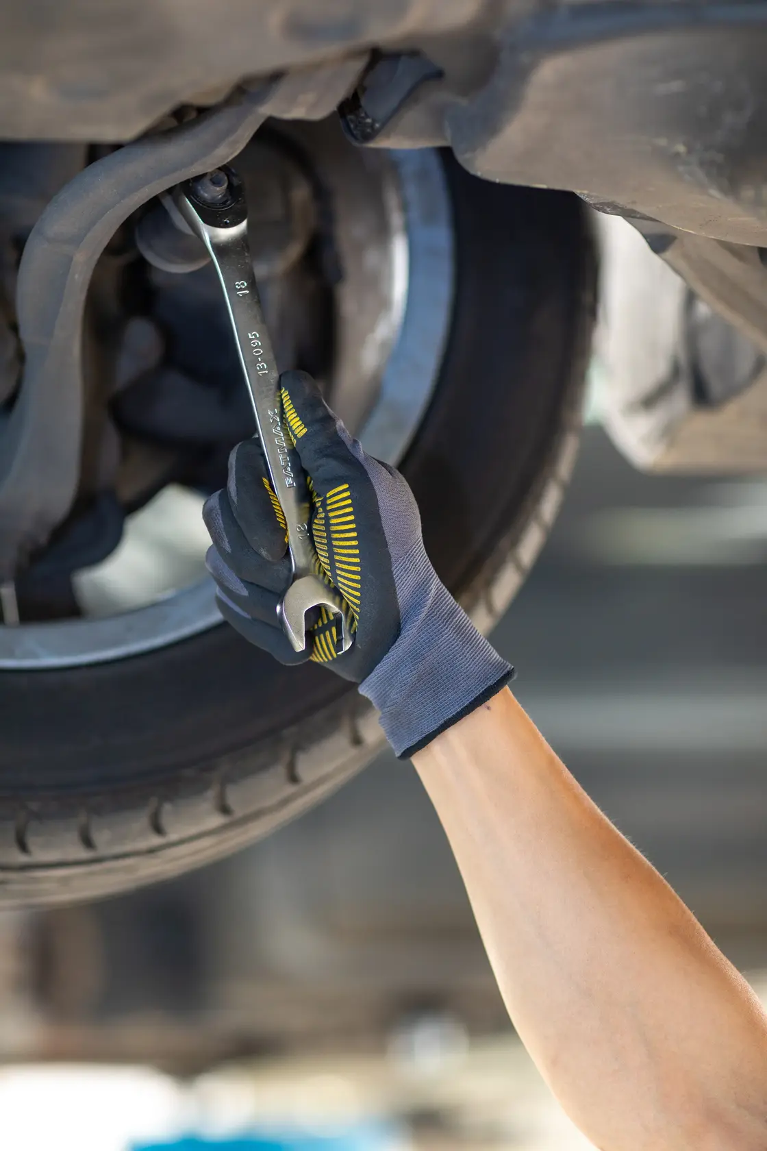 STANLEY FMMT13083-0 wrench held by gloved hand tightening bolt under car wheel, automotive repair photography.