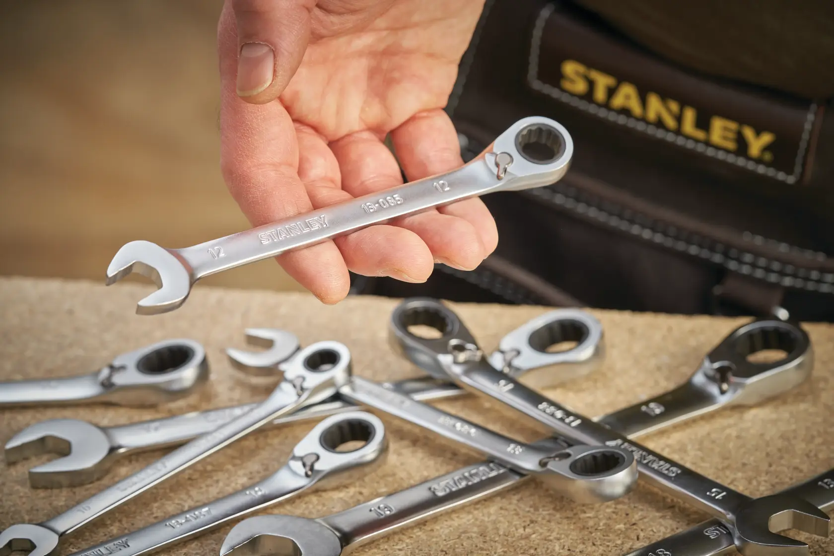 STANLEY FMMT13084-0 ratcheting wrench set, hand holding silver wrench, workshop surface.