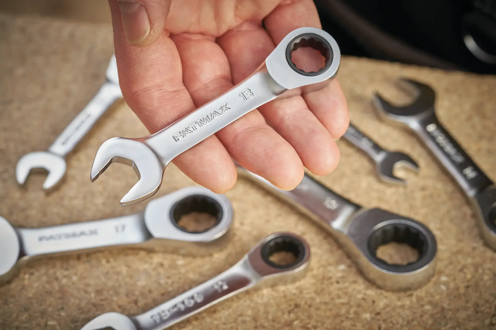 Photo of STANLEY FMMT13112-0 ratcheting spanners, close-up of hand holding a silver wrench, tools on work surface.