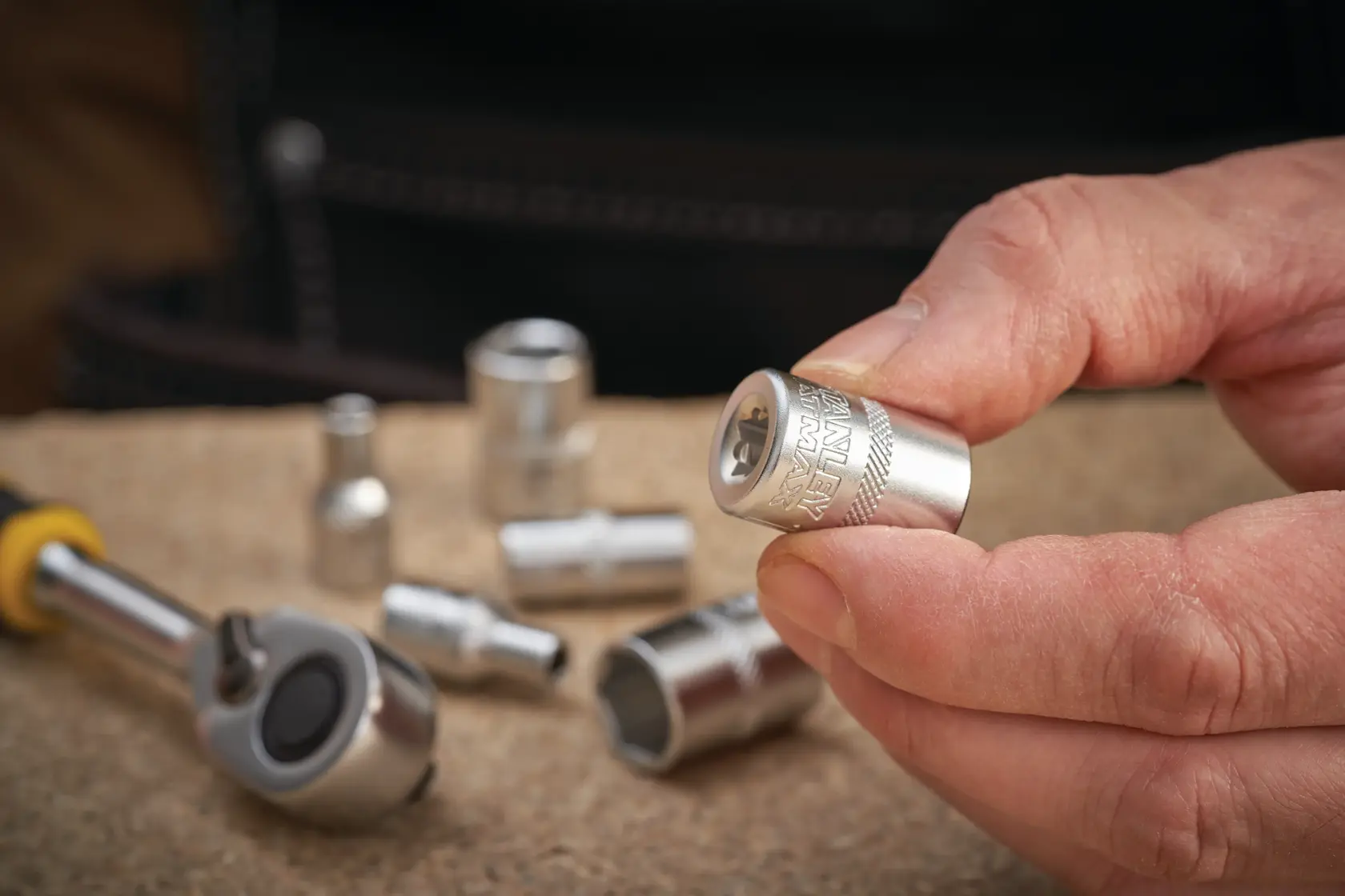 STANLEY FMMT17192-0 chrome socket held in hand with ratchet and sockets on workbench.