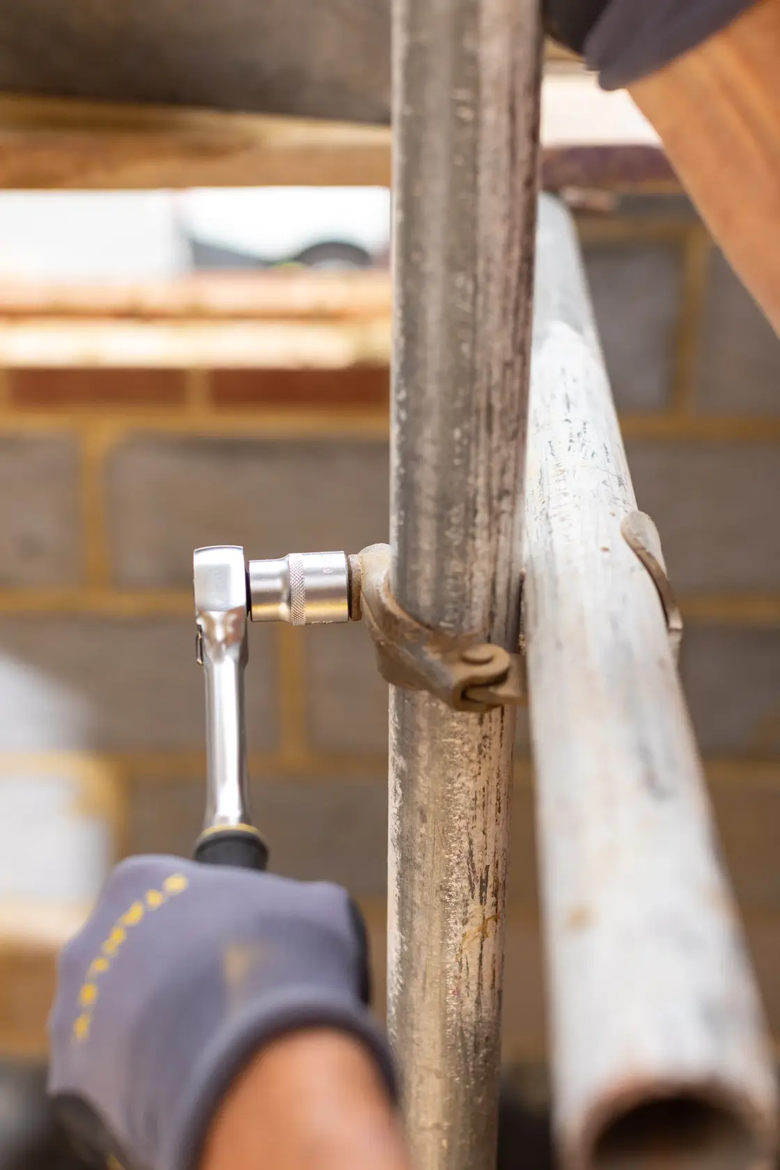 Photo of STANLEY FMMT17229-0 ratchet wrench tightening scaffold clamp outdoors.