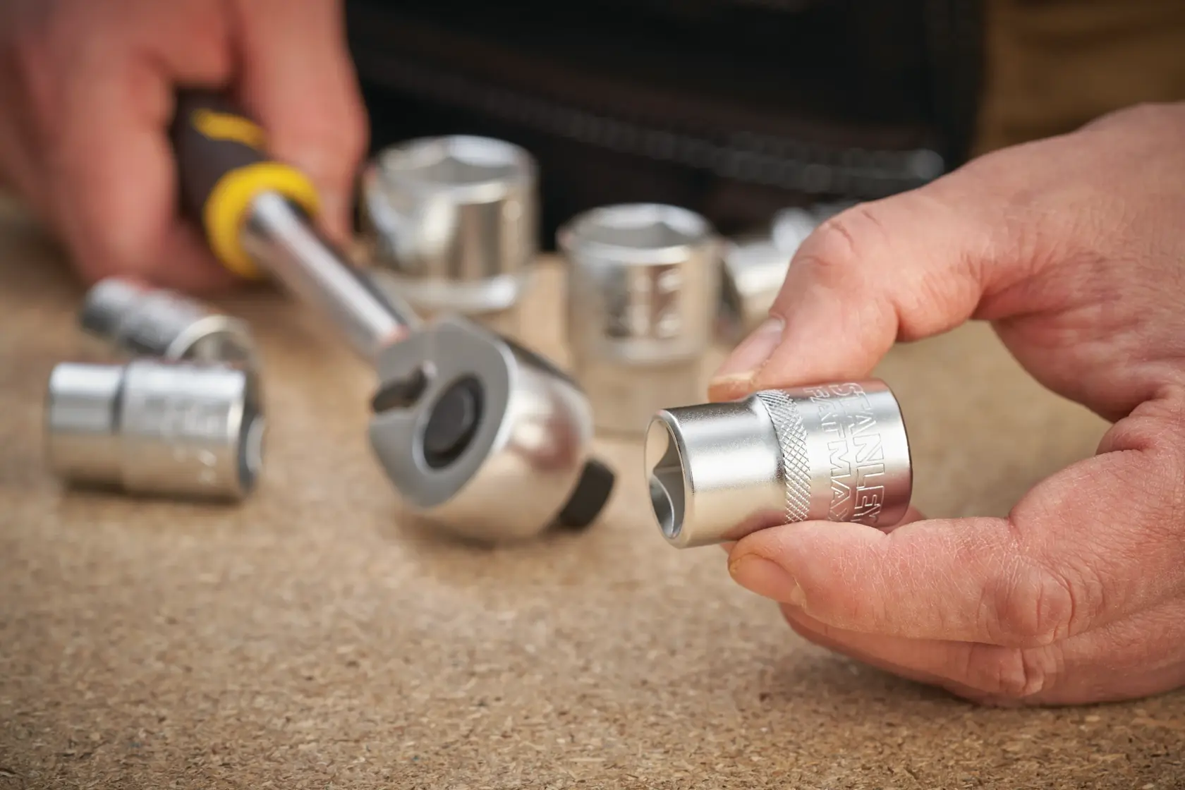STANLEY FMMT17246-0 socket set photography with hand holding a chrome socket and ratchet tool on a work surface.