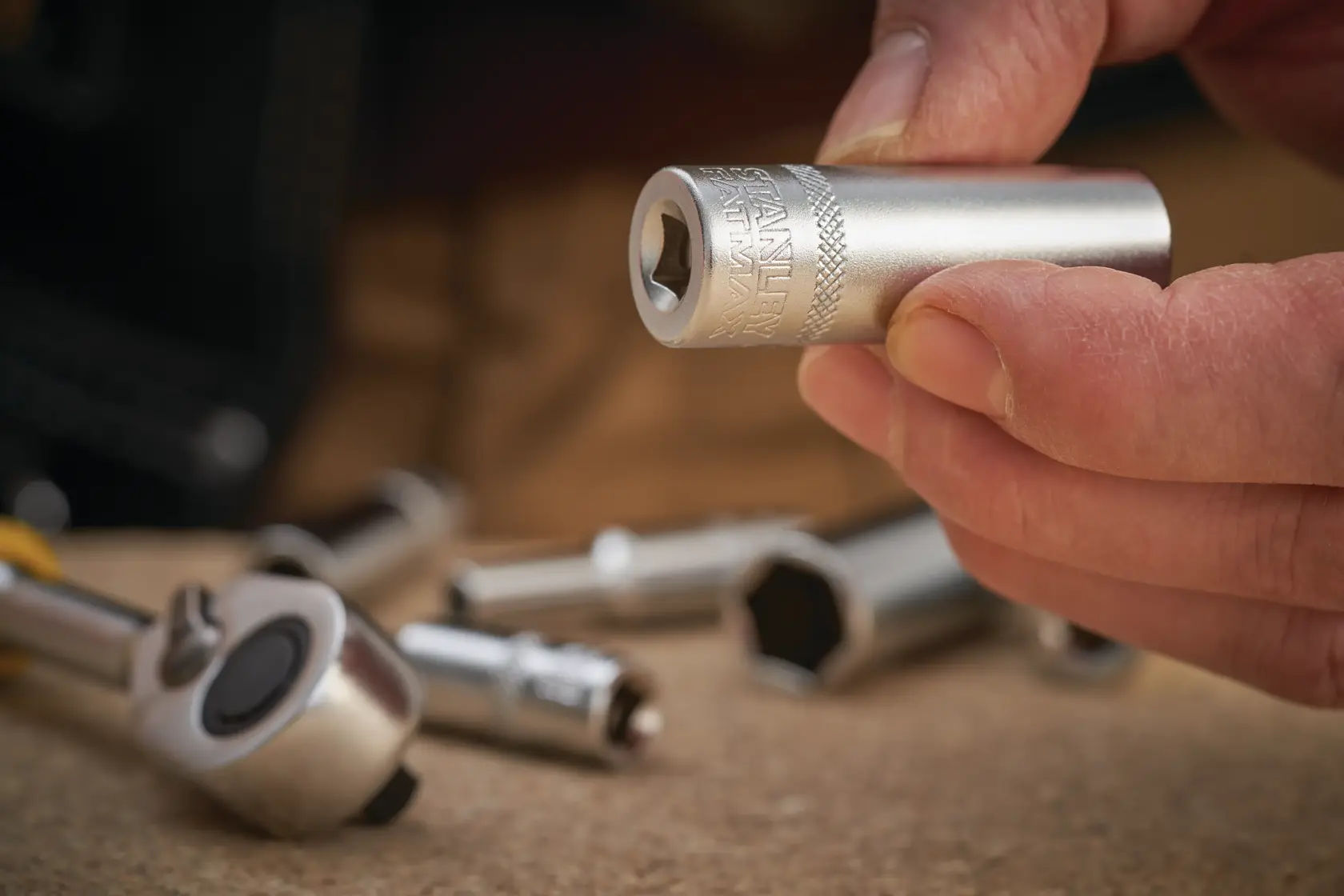 STANLEY FMMT17963-0 chrome socket held in hand, with ratchet and other sockets in background, close-up photo.
