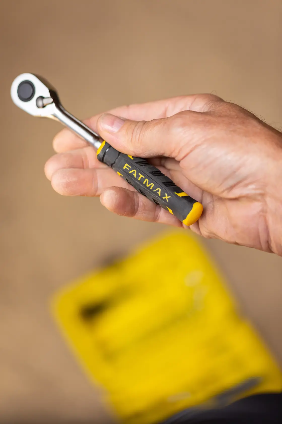 STANLEY FMMT82676-0 hand holding compact black and yellow ratchet wrench, FATMAX branding visible.