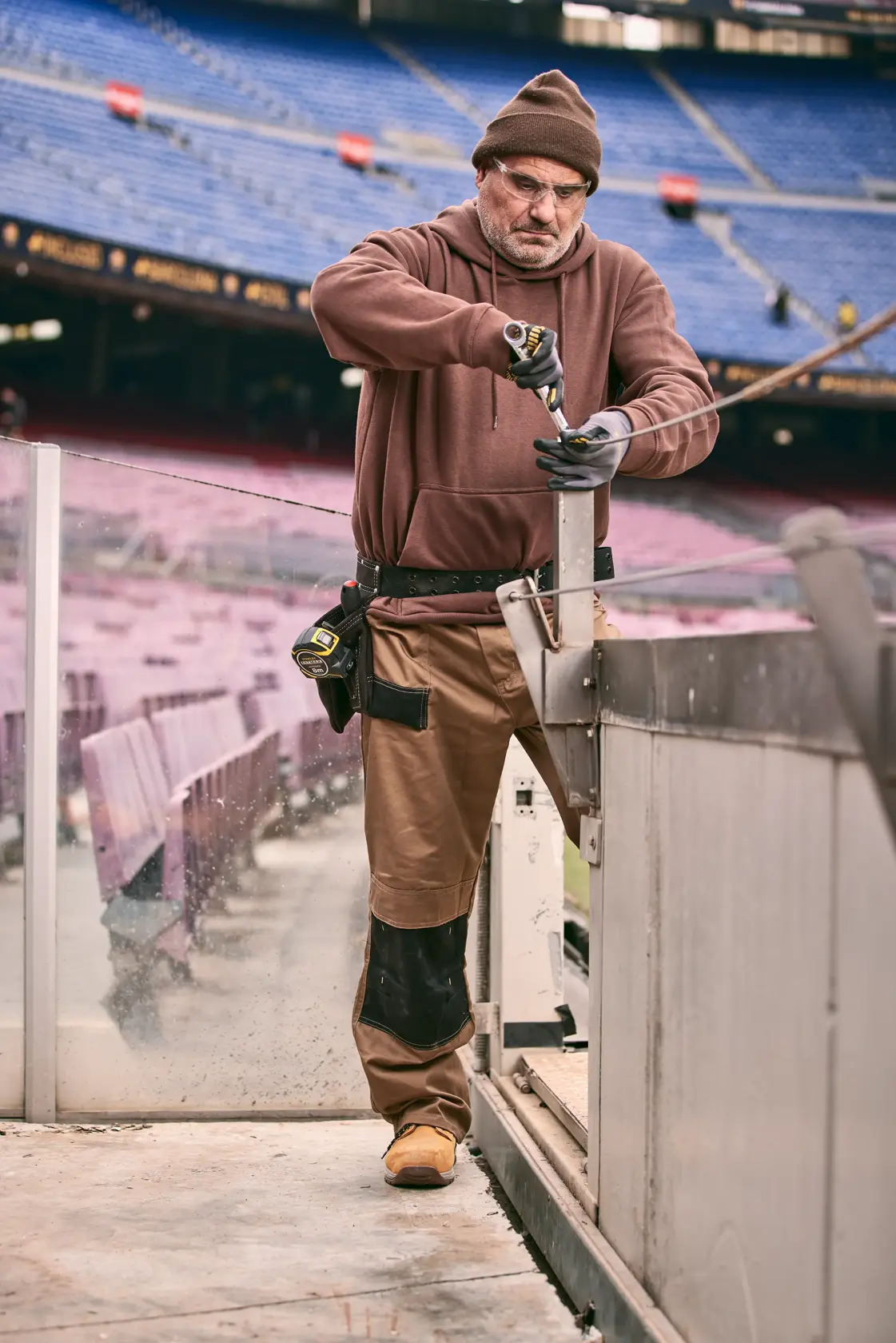 Photo of worker using STANLEY FMMT82848-0 screwdriver at stadium, wearing tool belt and gloves.