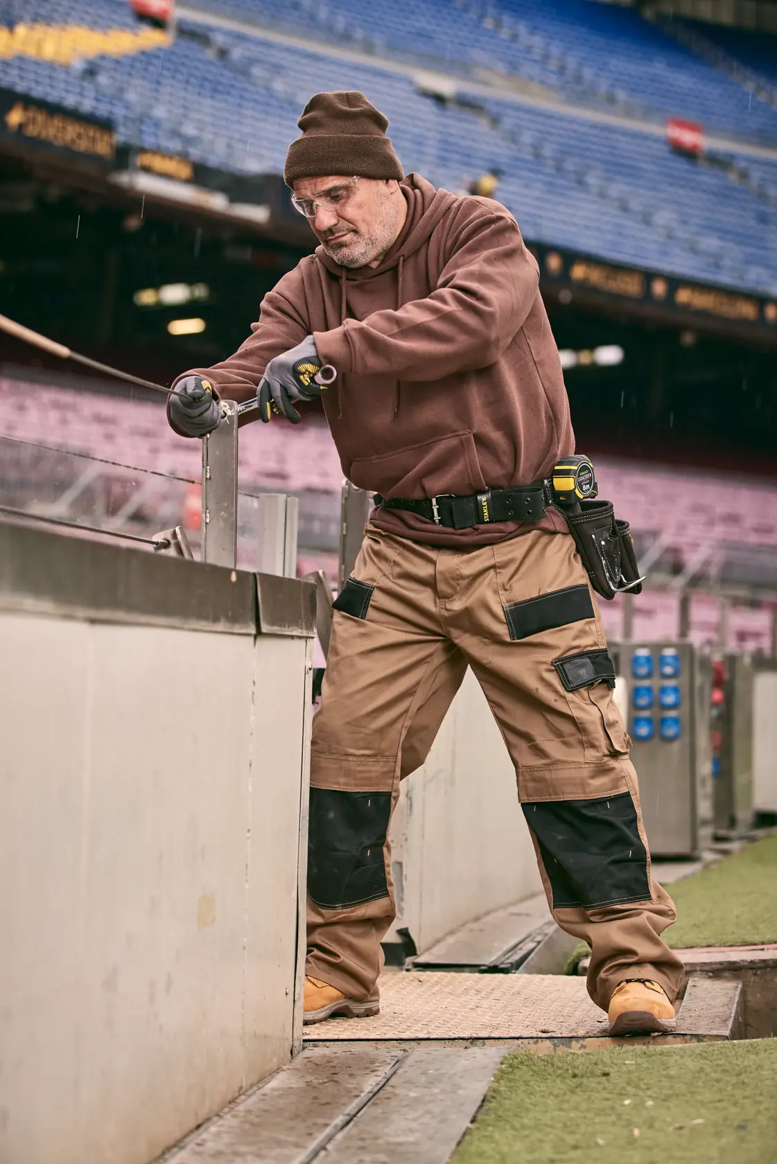 STANLEY FMMT82848-0 professional holding tool, wearing tool belt and work pants, at stadium construction site.