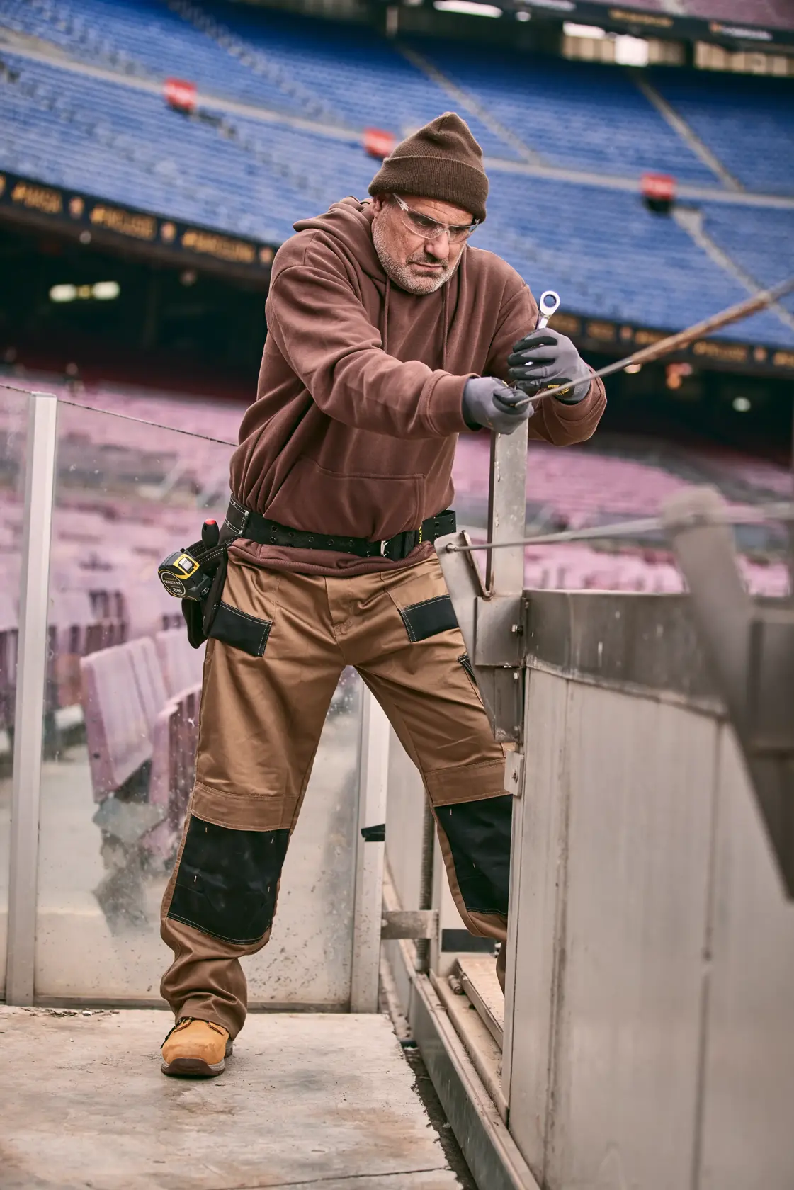STANLEY FMMT82848-0 photography of a worker in brown workwear using a hand tool in an empty stadium.