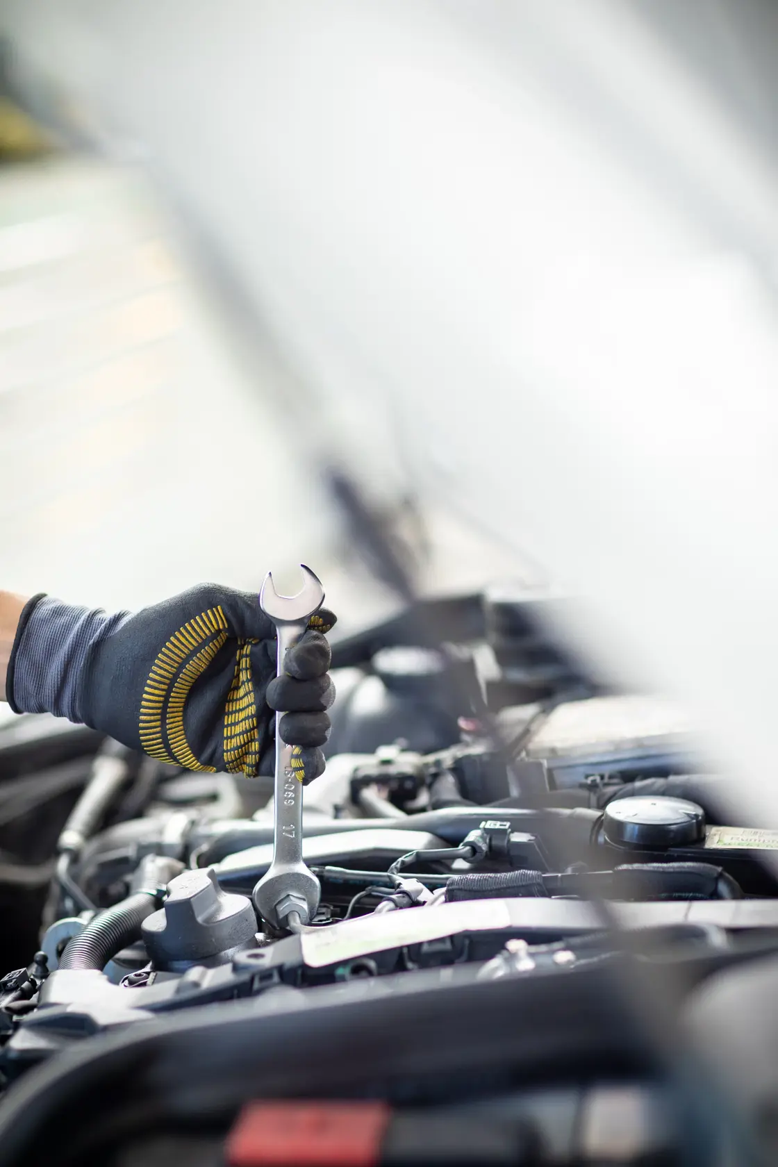 STANLEY FMMT82901-0 wrench in gloved hand tightening bolt in car engine bay, side angle, photography.