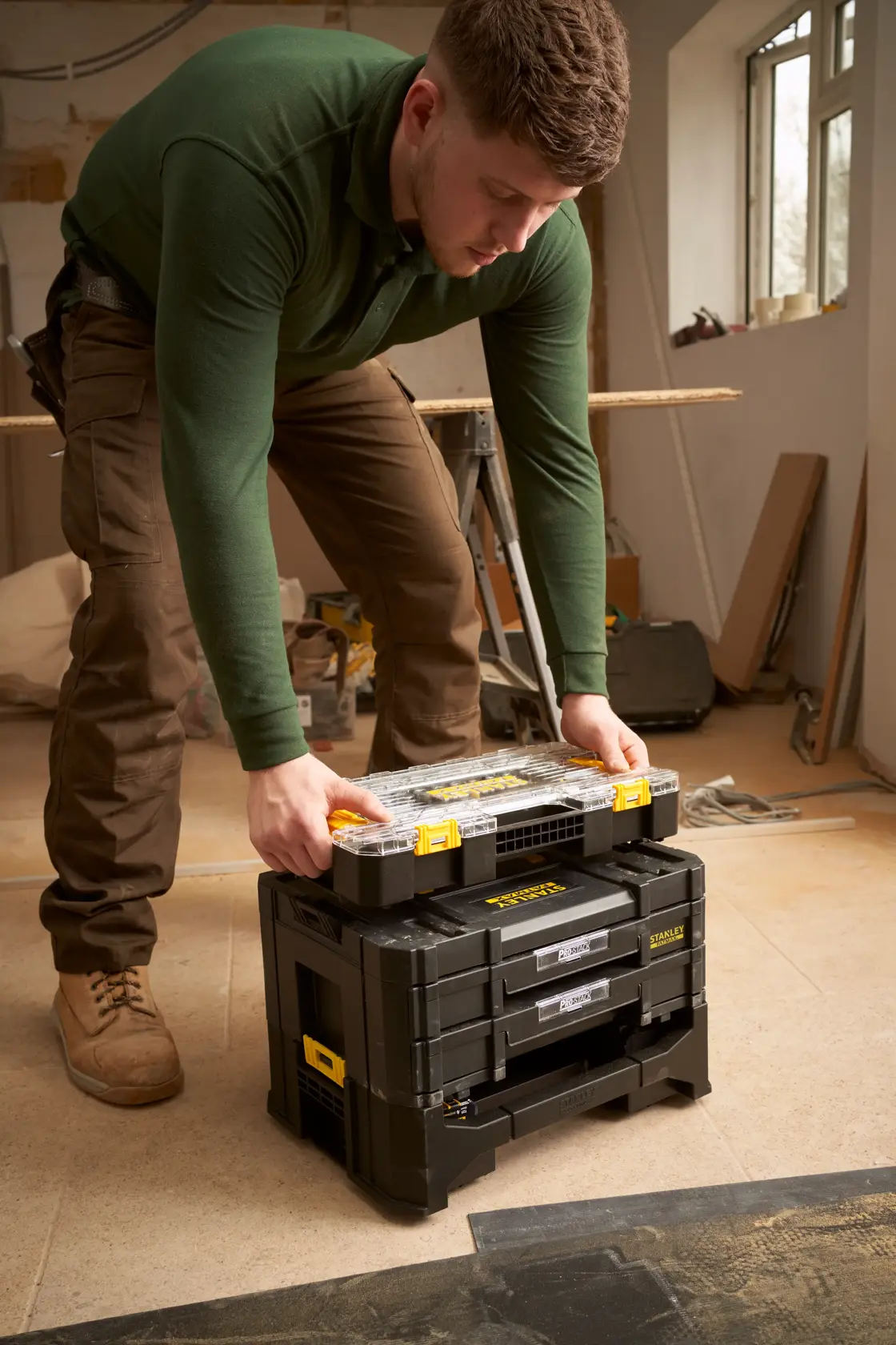 STANLEY FMMT98103-1 modular black toolbox set with yellow accents in workshop, person stacking organizer on top.